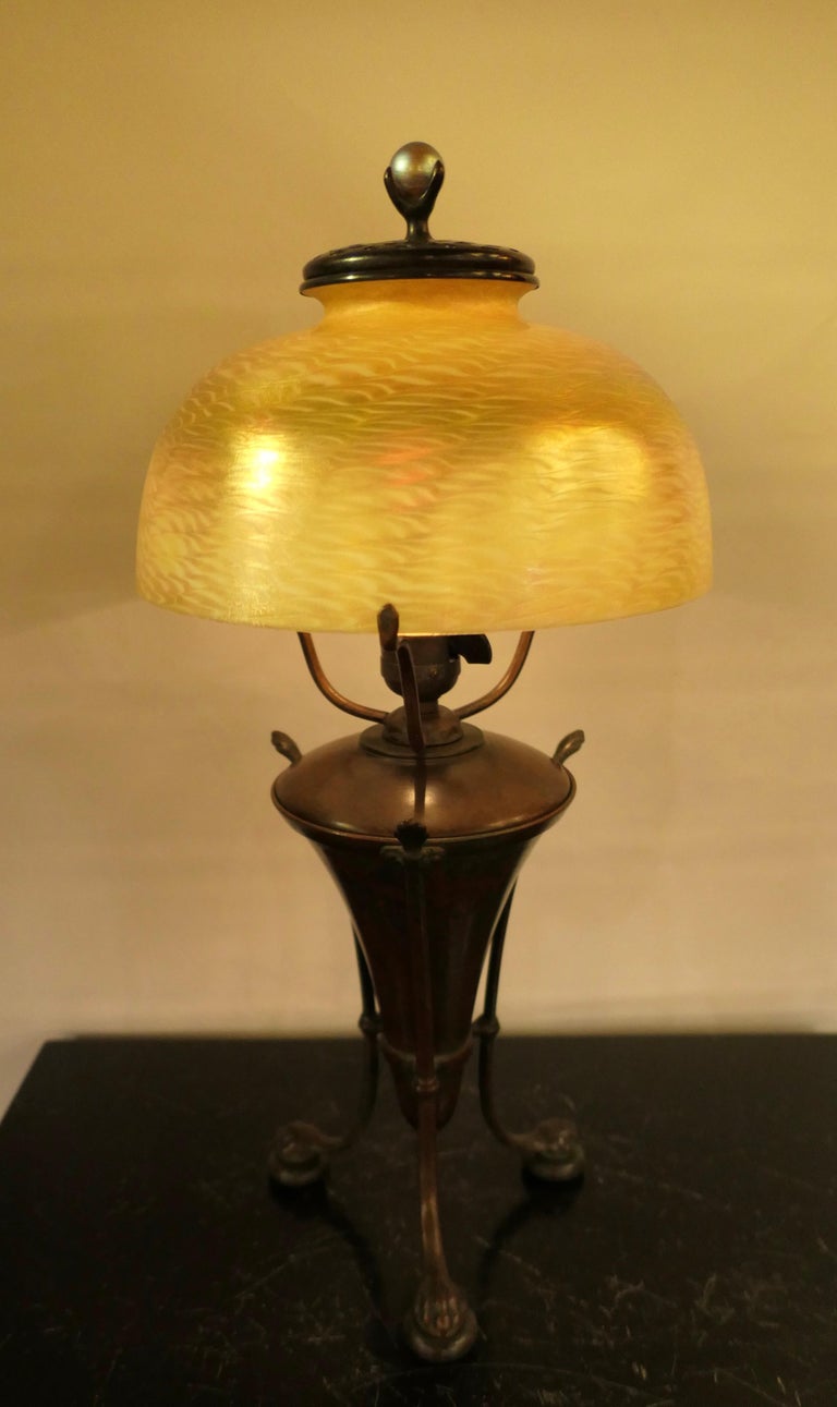 This stunning vintage original Tiffany Studios, New York table lamp dates from the very early 20th century. The vividly colored damascene favrile art glass shade rests upon an early patinated classic urn base. This base is designed with three