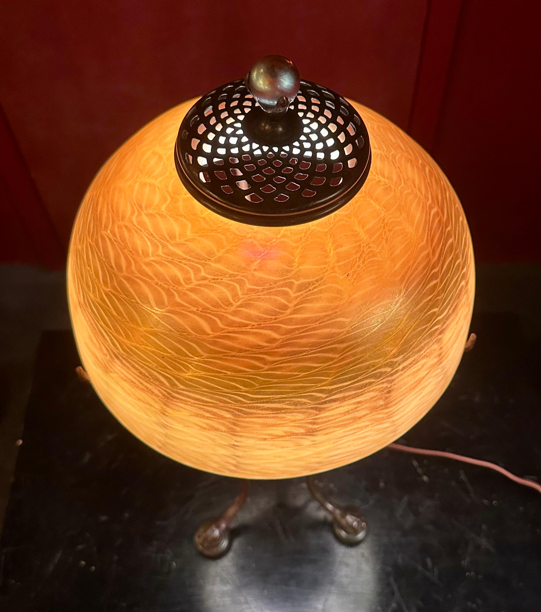 This stunning vintage original Tiffany Studios, New York table lamp dates from the very early 20th century. The vividly colored damascene favrile art glass shade rests upon an early patinated classic urn base. This base is designed with three