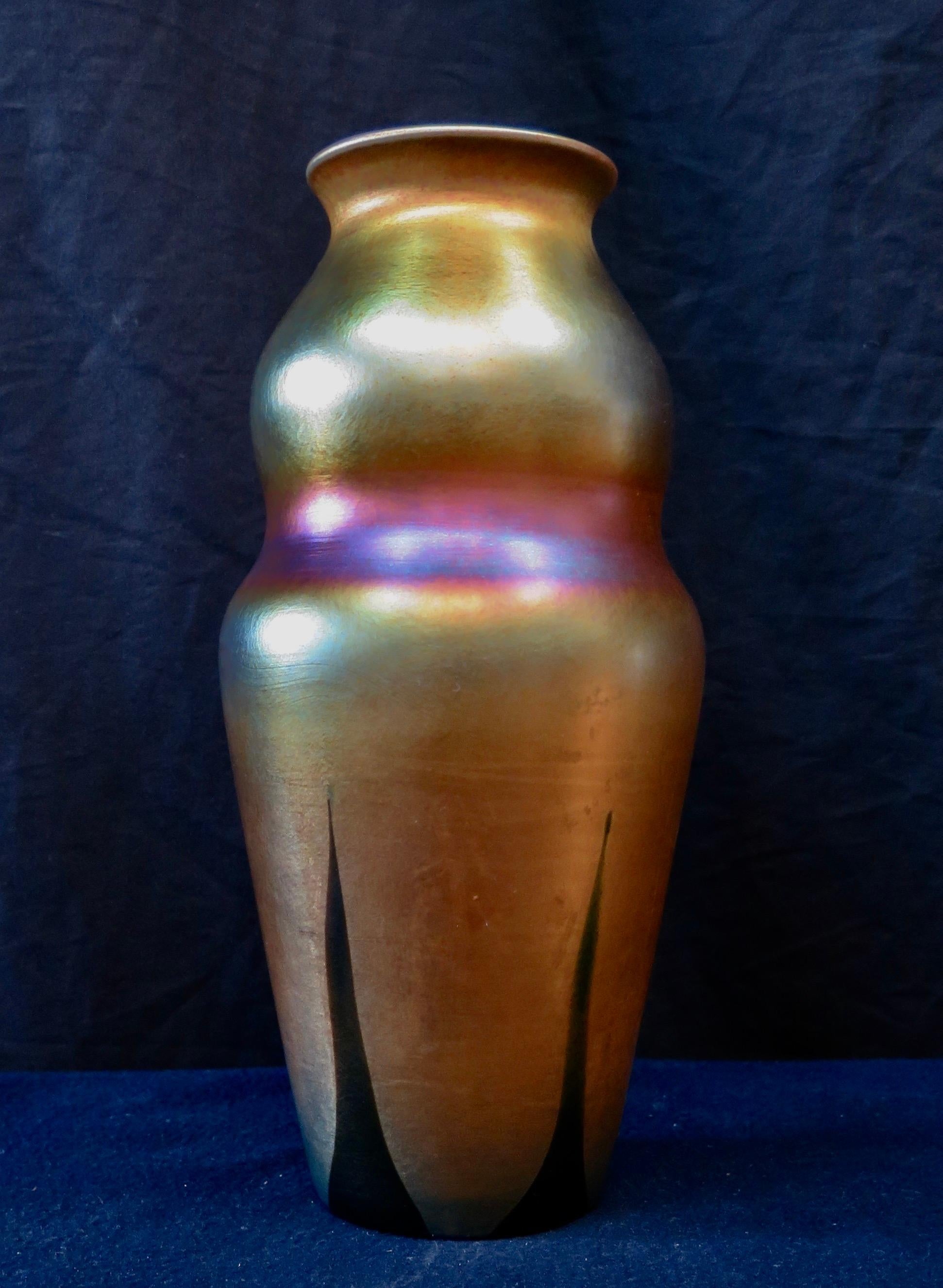 This stunning Tiffany Studios gold vase is decorated & dates from the early 1900’s. The hand blown vase is accented with five elongated green feather “tips” from “feathers” that originate on the undersurface of the vase. Looking at this