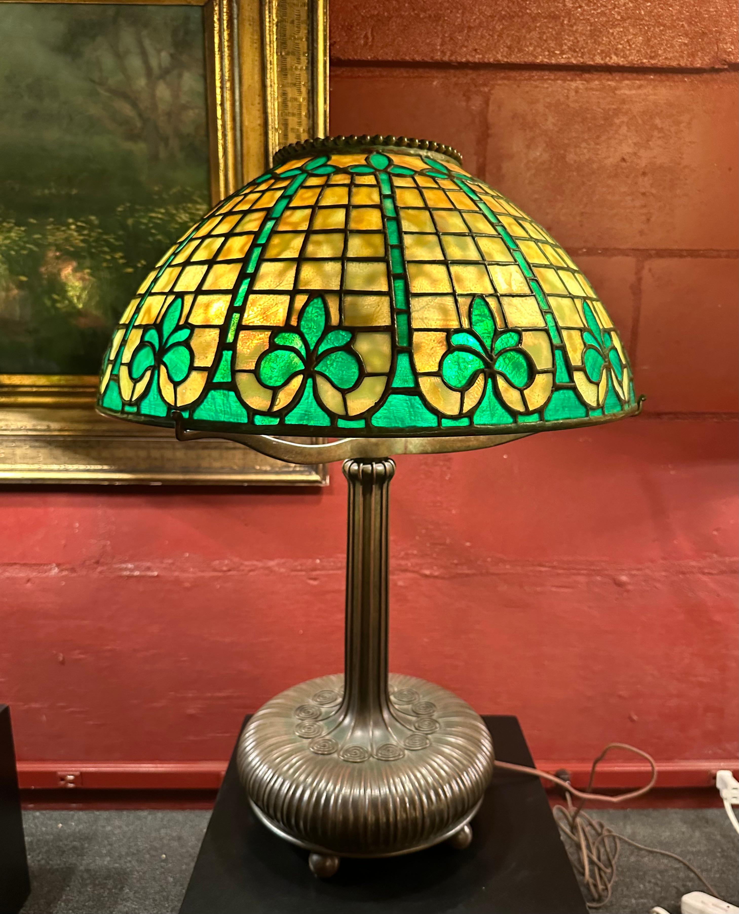 This beautiful early Tiffany Studios 16” geometric lamp shade is enhanced with a band of bright green Fleur de Lis symbols circling the lowest part of the shade.Each of these symbols is separated with a leaded column of bright green tiles. The shade