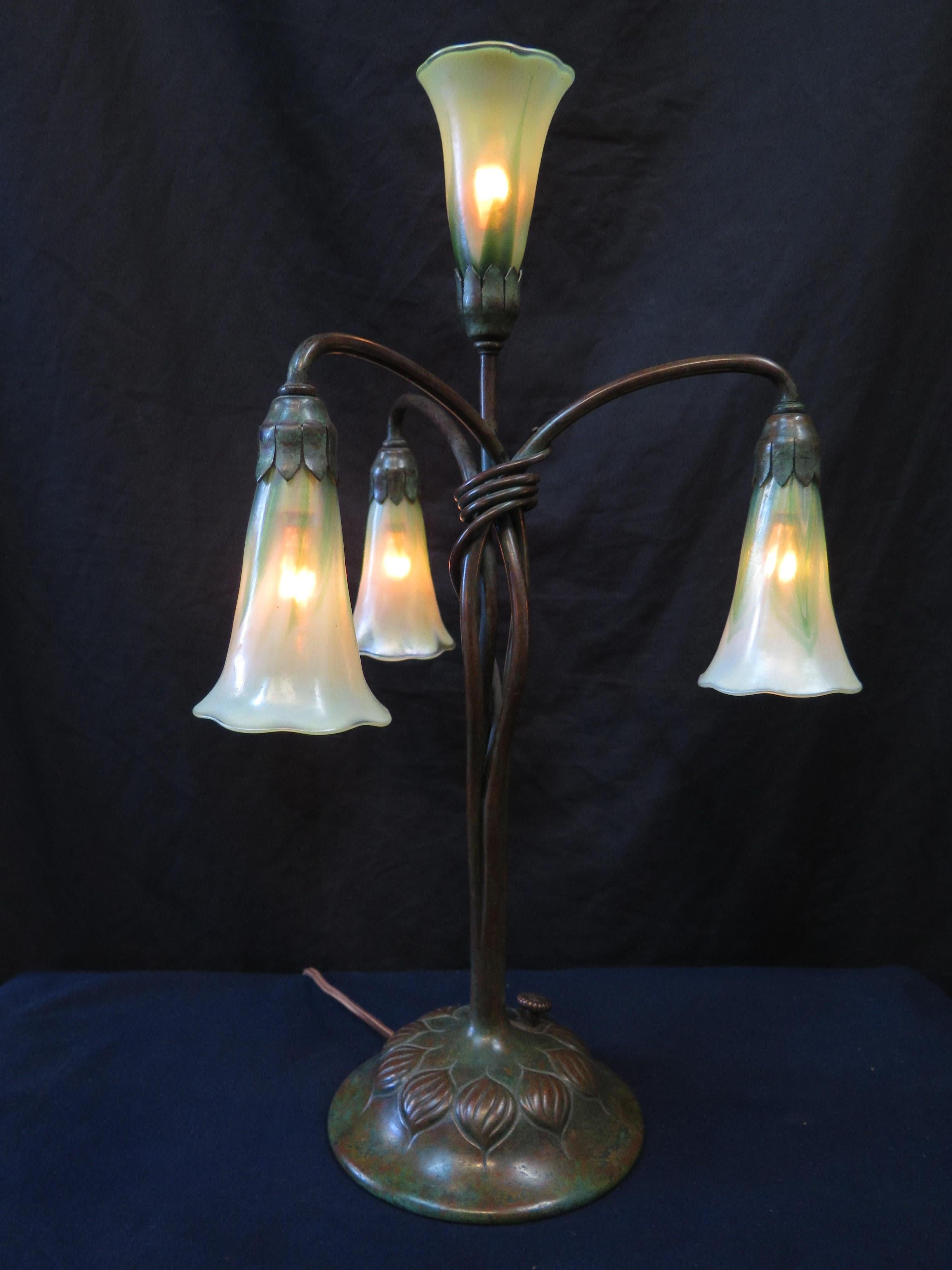 Diese frühe vierflammige Lilien-Tischlampe wurde in den frühen 1900er Jahren von den Tiffany Studios in New York hergestellt. Der stilvolle Sockel aus patinierter Bronze ist mit einem Zwiebelmotiv verziert und weist vier anmutige röhrenförmige