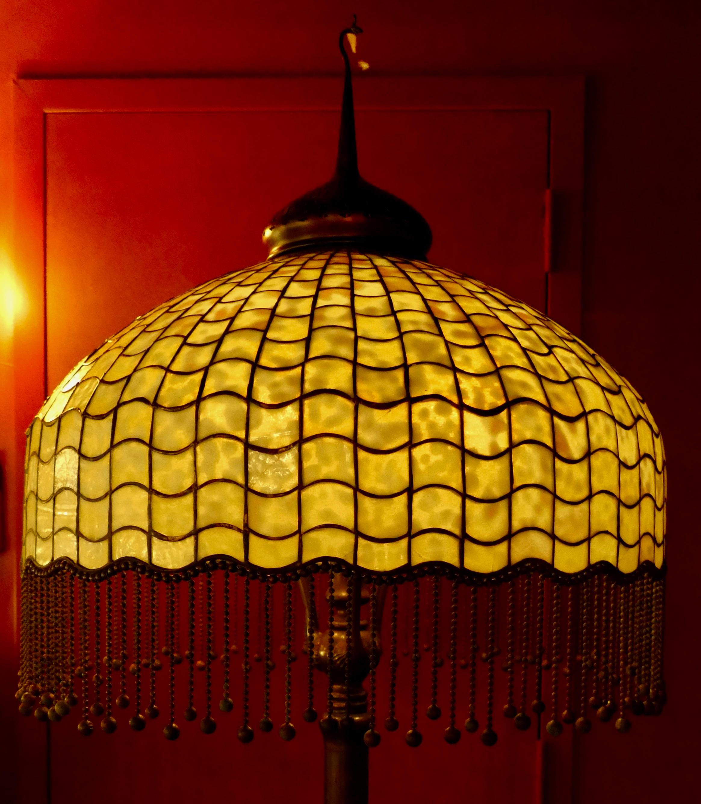 This stylish original Tiffany Studios floor lamp dates from the early 20th century. The wonderful yellow/cream color geometric lampshade features mottled glass & the undulating bottom edge has a beautiful fringe attached that enhances the patinated