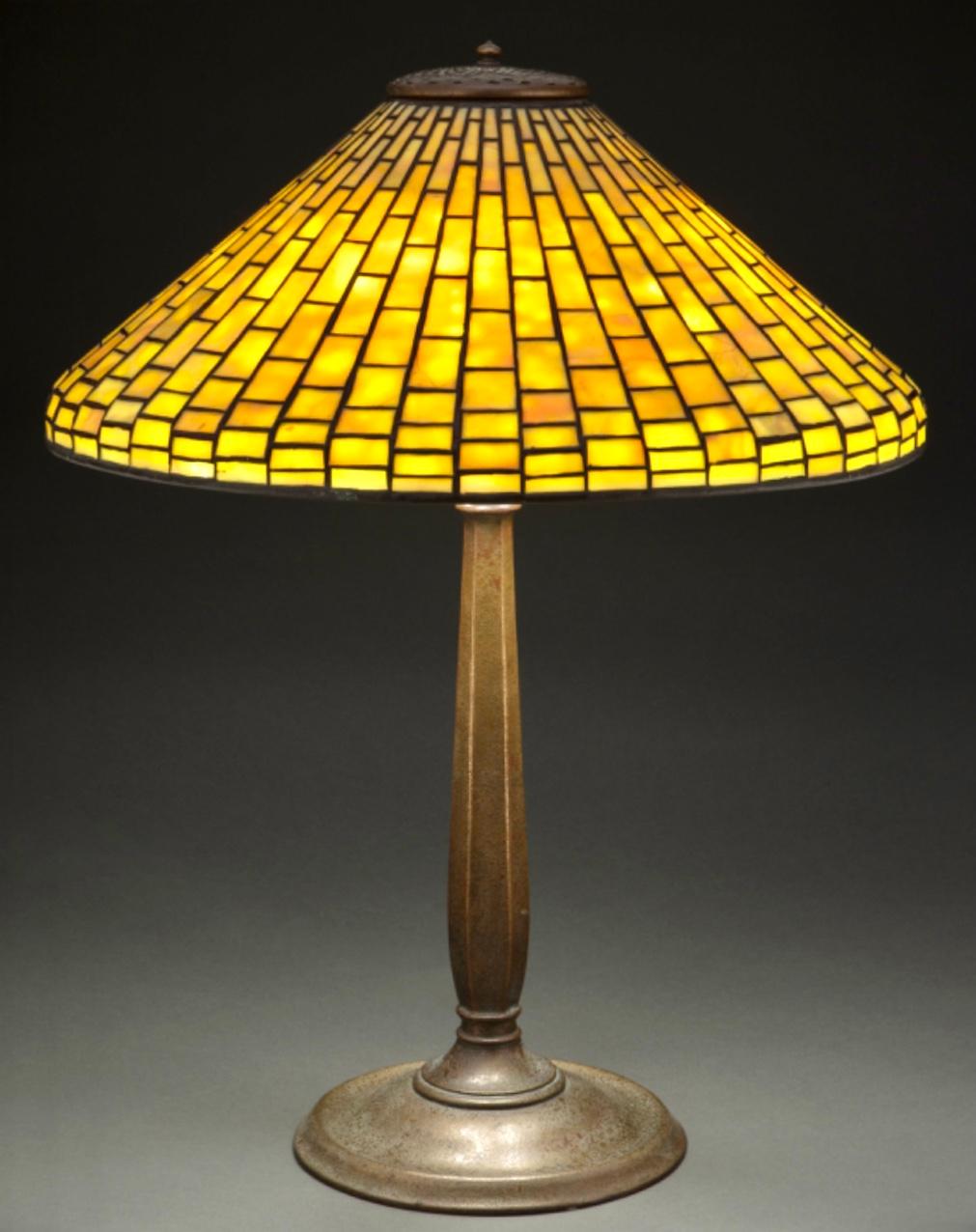 Geometrische Tischlampe aus Bleiglas und patinierter Bronze der Tiffany Studios, um 1910. Jugendstil-Klassiker mit Art-Déco-Design. Attraktive Orangenschalenstruktur mit leichter Vergoldung und rot gefärbtem Bronzesockel, gekrönt von einem
