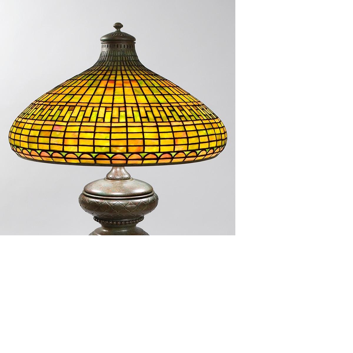 A Tiffany Studios New York glass and bronze “Geometric” table lamp, featuring a mottled orange, yellow and green leaded glass shade atop an intricately sculpted patinated bronze base.

Pictured in: Tiffany at Auction by Alastair Duncan, Rizzoli