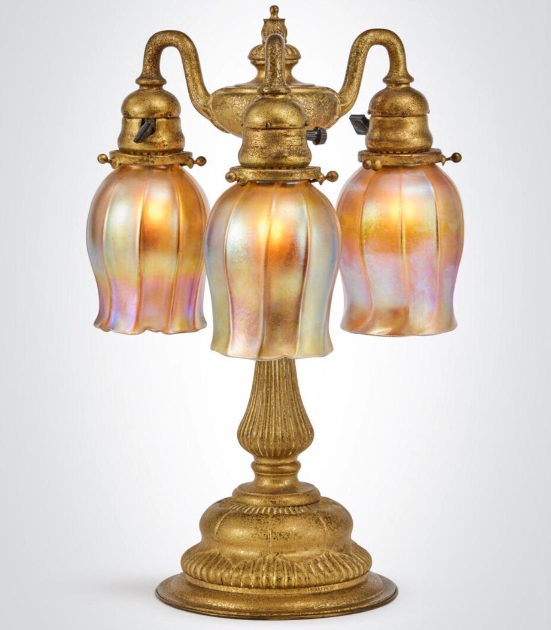 Tiffany Studios Three-Light Table Lamp
circa 1910
favrile glass shades, Three arm gilt bronze base
Shades engraved “L.C.T. Favrile”
Base impressed “TIFFANY STUDIOS/NEW YORK/309”
Height: 16.5 Inches (41.9 cm) 
Width: 11 Inches

Condition:
