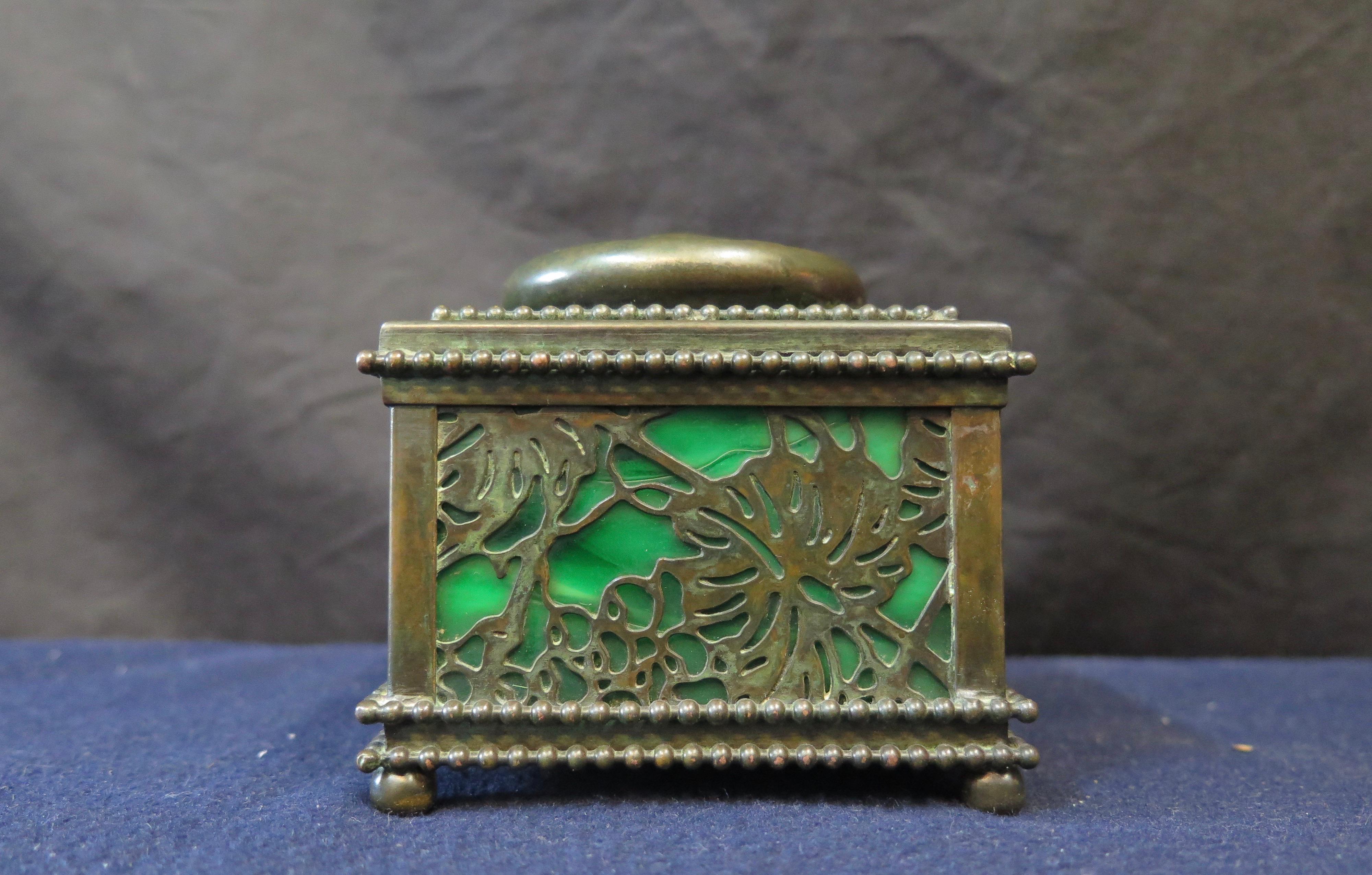 This vintage Tiffany Studios patinated brass & favrile art glass inkwell is beautifully designed in the desirable “grapevine” pattern & dates from the early 1900’s. It retains its original green & white favrile glass covered by a grapevine brass