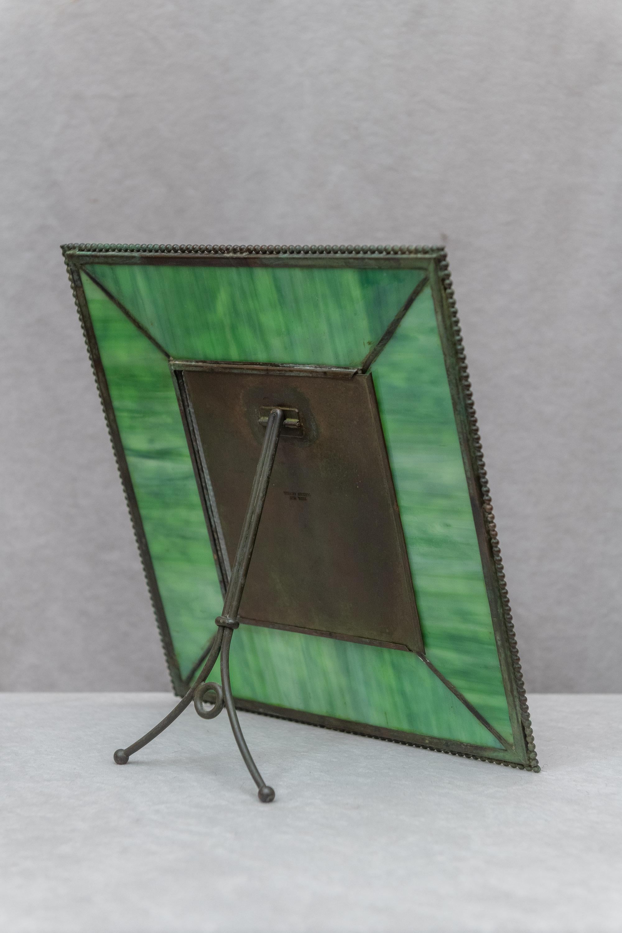 This is an original signed Tiffany Studios grapevine pattern picture frame. Please note the rich green background glass. We did light up the glass in some of our photos, and you can certainly do the same when you get it home. A very desirable and