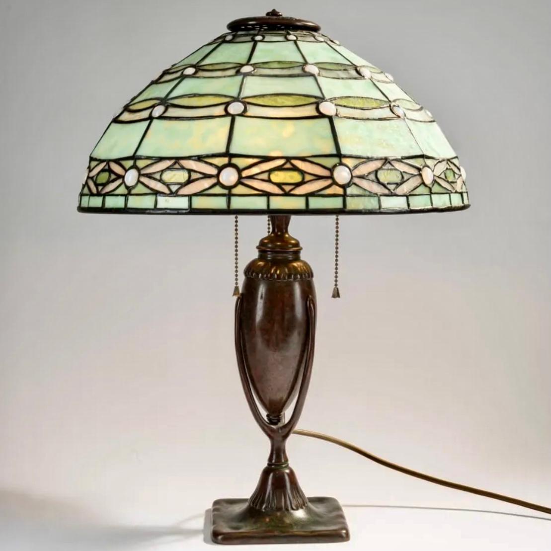 Tiffany Studios, New York, 'Jeweled Blossom' table light, c. 1907

Height: 21.5 Inches (55 cm)
Diameter: 16 inches (40.2 cm)

Leaded opal glass with some white cabochons, mainly in green and opal white tones. Ribbons with stylized flowers. Lead