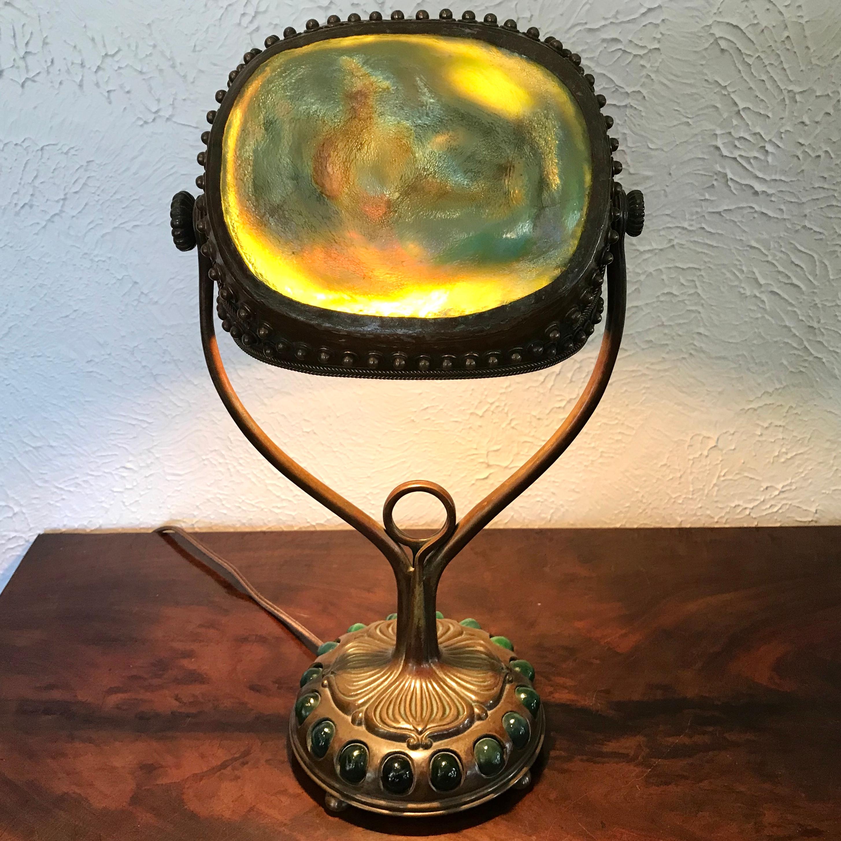 Tiffany Studios jeweled turtleback desk lamp, Circa 1900
A Tiffany Studios bronze table lamp base decorated with jeweled green favrile swirl glass balls supporting the turtleback shade with green iridescent turtlebacks showing flashes of purple,