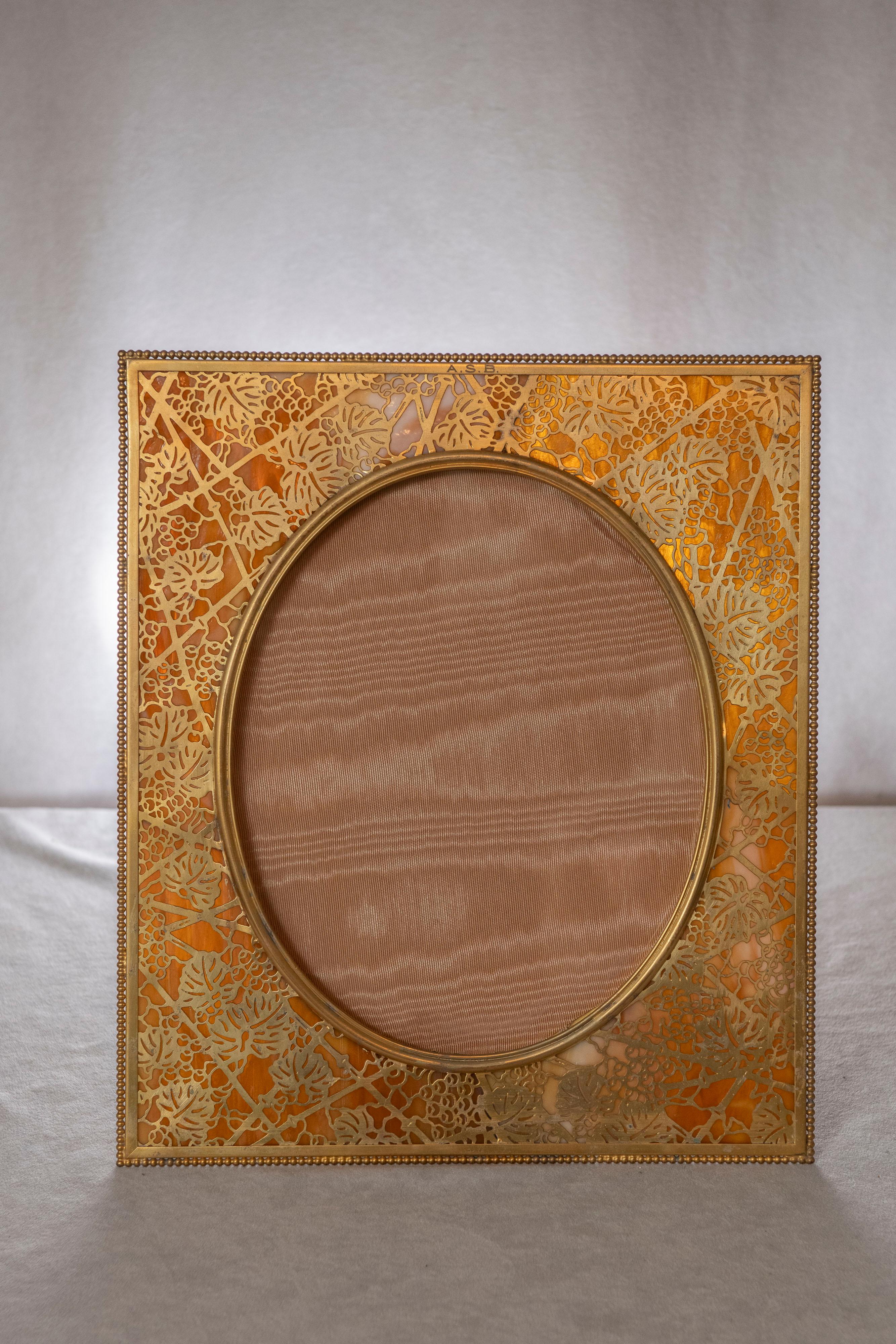 Dieser große und schöne Bilderrahmen ist das Werk der Tiffany Studios. Dies ist das Weinrebenmuster mit vergoldeter Oberfläche. Reichhaltiges Tiffanyglas hebt den Rahmen hervor, der die Rückseite der filigranen Arbeit bedeckt. Ordnungsgemäß