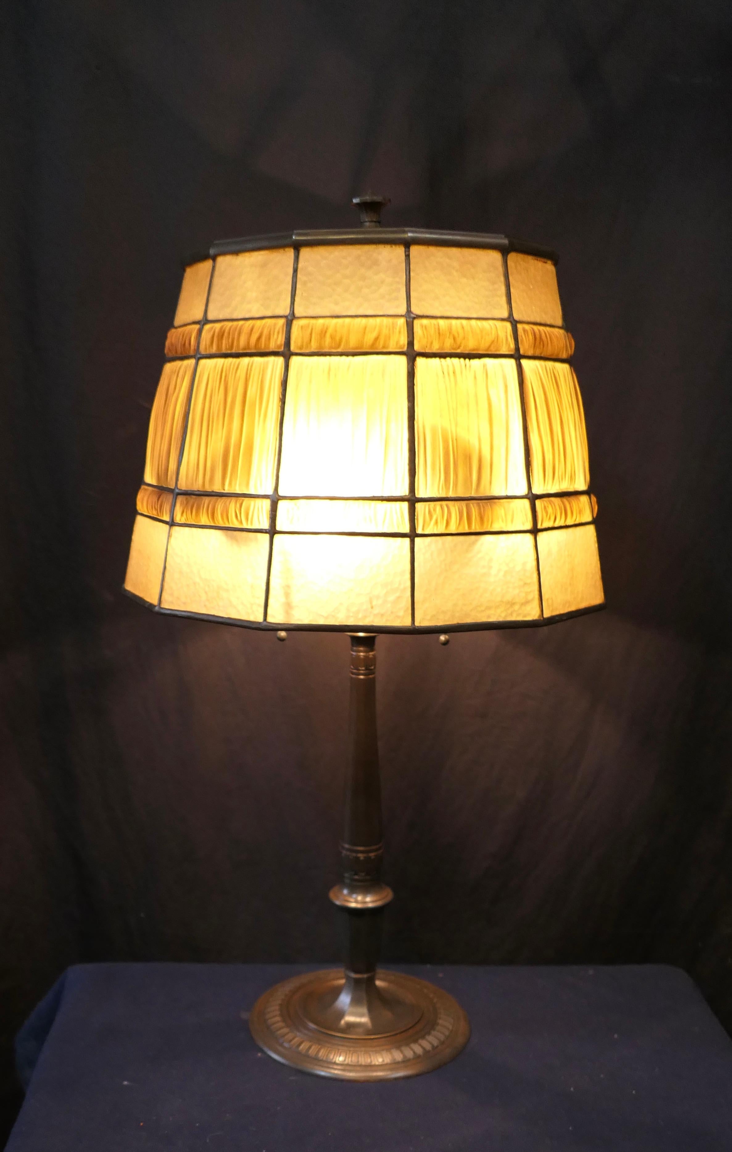 This vintage early 20th century patinated bronze table lamp is beautifully designed with an art glass linenfold shade. The barrel shape paneled shade features golden amber color favrile art glass panel above & below pleated, textured what Tiffany