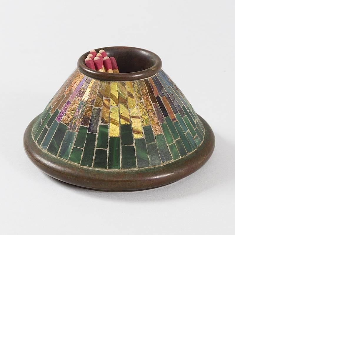 A Tiffany Studios New York Art Nouveau mosaic match holder. The item features vertical panels of mosaic iridescent glass in blues, greens, pinks and yellows over a patinated bronze body, circa 1900

This item is pictured in: Tiffany Desk Sets, by