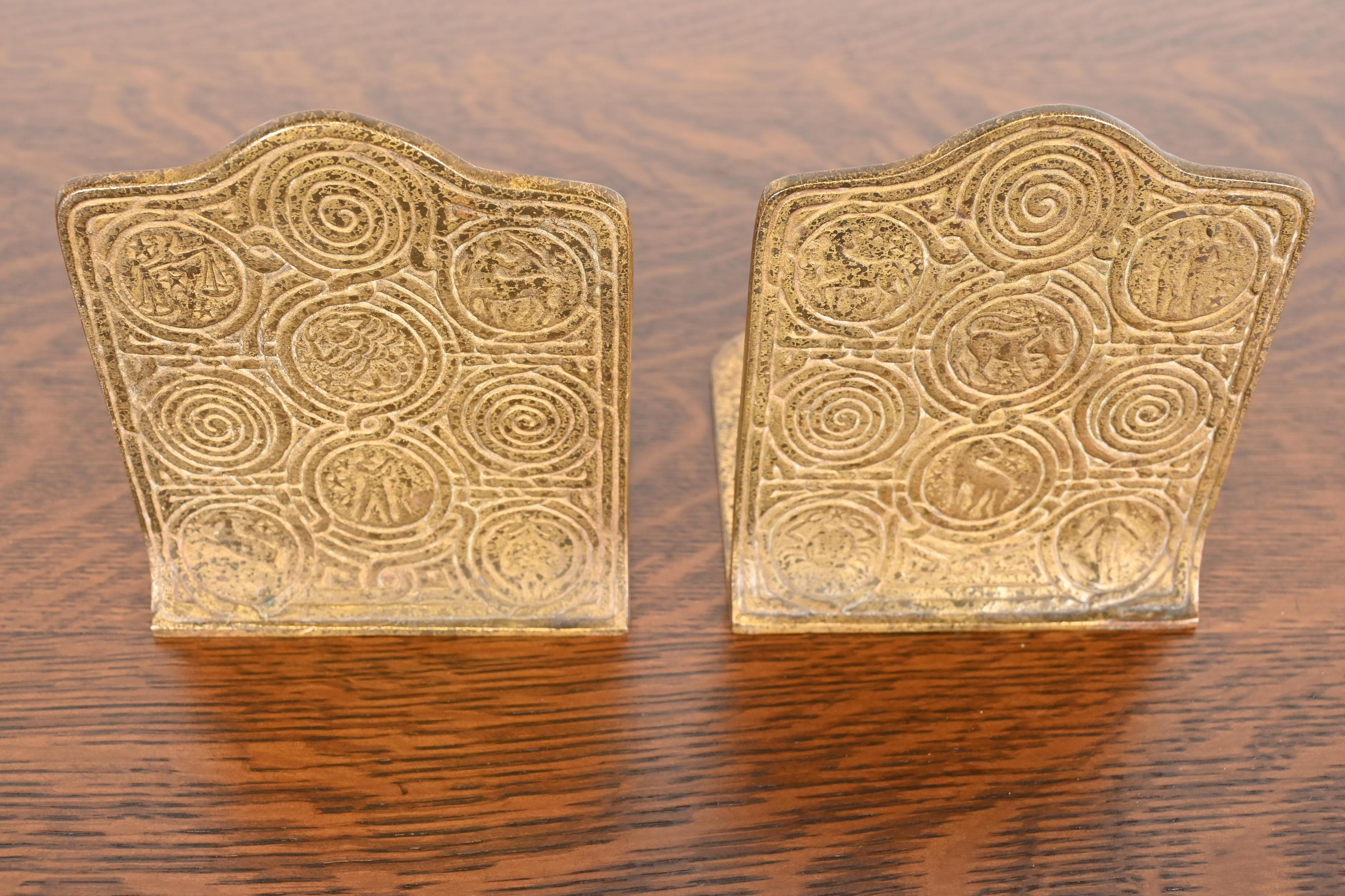 Magnifique paire de serre-livres en bronze doré d'époque Arts & Crafts ou Art Deco, ornés de motifs du Zodiac.

Par Tiffany Studios

New York, États-Unis, début du XXe siècle

Chacune mesure : 5 