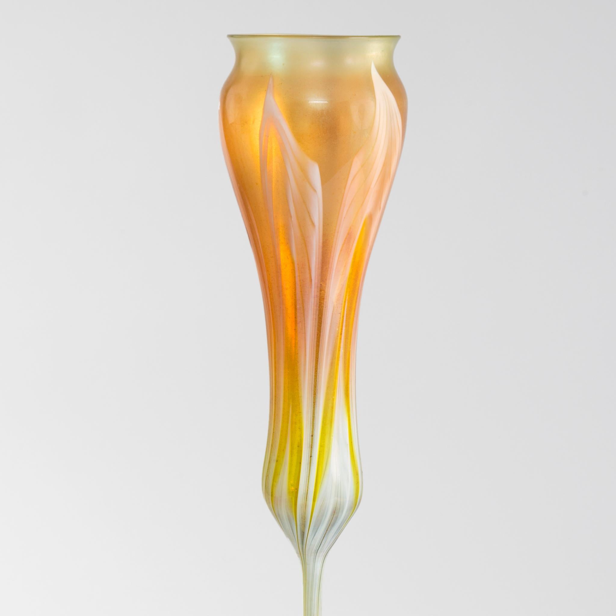 This Favrile glass flower form vase, by Tiffany Studios New York, is meant to suggest the calyx forms, open or closed, of crocus or tulip flowers. This richly-hued orange-yellow vase is tall and slender and colored with exquisite green and white