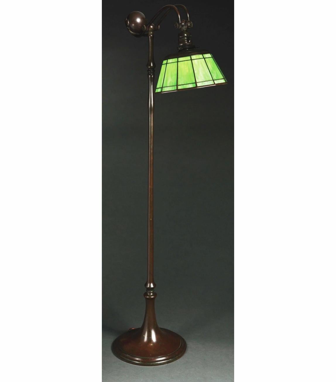 A Tiffany Studios counter balance floor lamp with a leaded green slag glass shade. Shade is 12 sided, each side with a large central panel, and smaller panel above and below. Top of shade in patinated bronze with pattern of “J” shaped