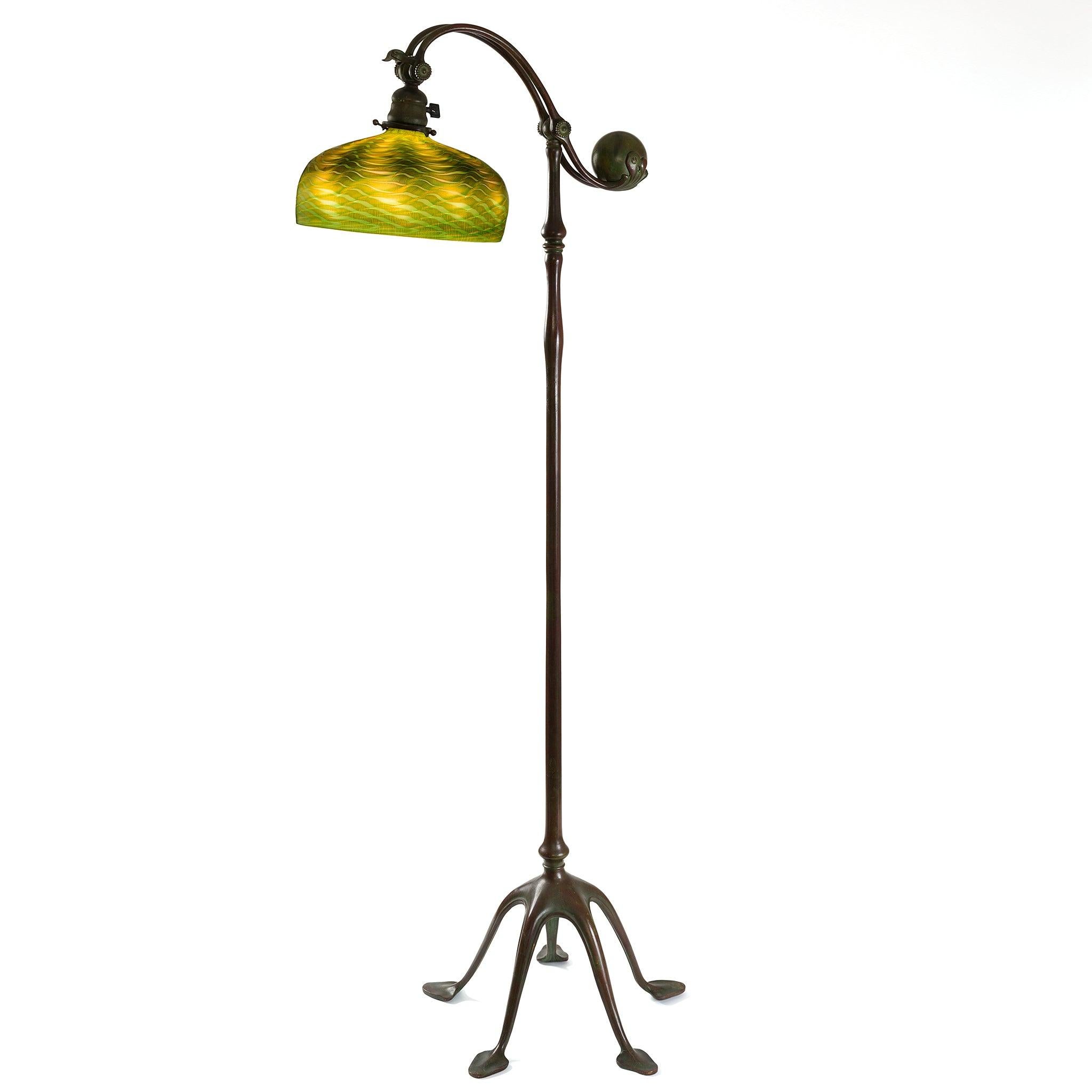This Tiffany Studios “Counter Balance” floor lamp features a green and gold iridescent damascene shade, which may be raised or lowered, and five-footed patinated bronze base. The green and gold damascene domed shade, with an upper band of