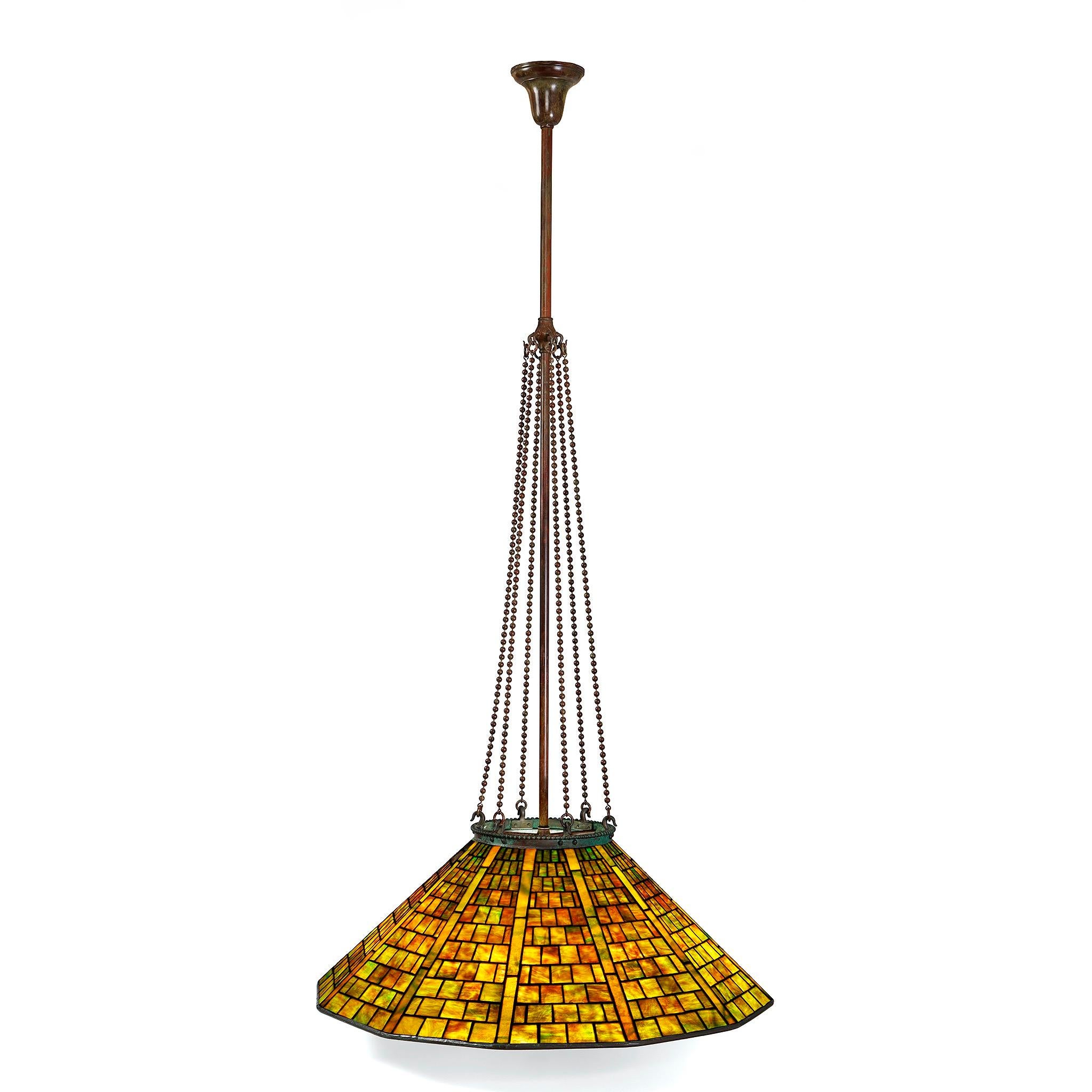 This exquisite 12-sided chandelier, crafted by Tiffany Studios New York, is a striking example of early 20th-century American design and craftsmanship. Suspended elegantly by six patinated bronze chains, the fixture exudes both strength and