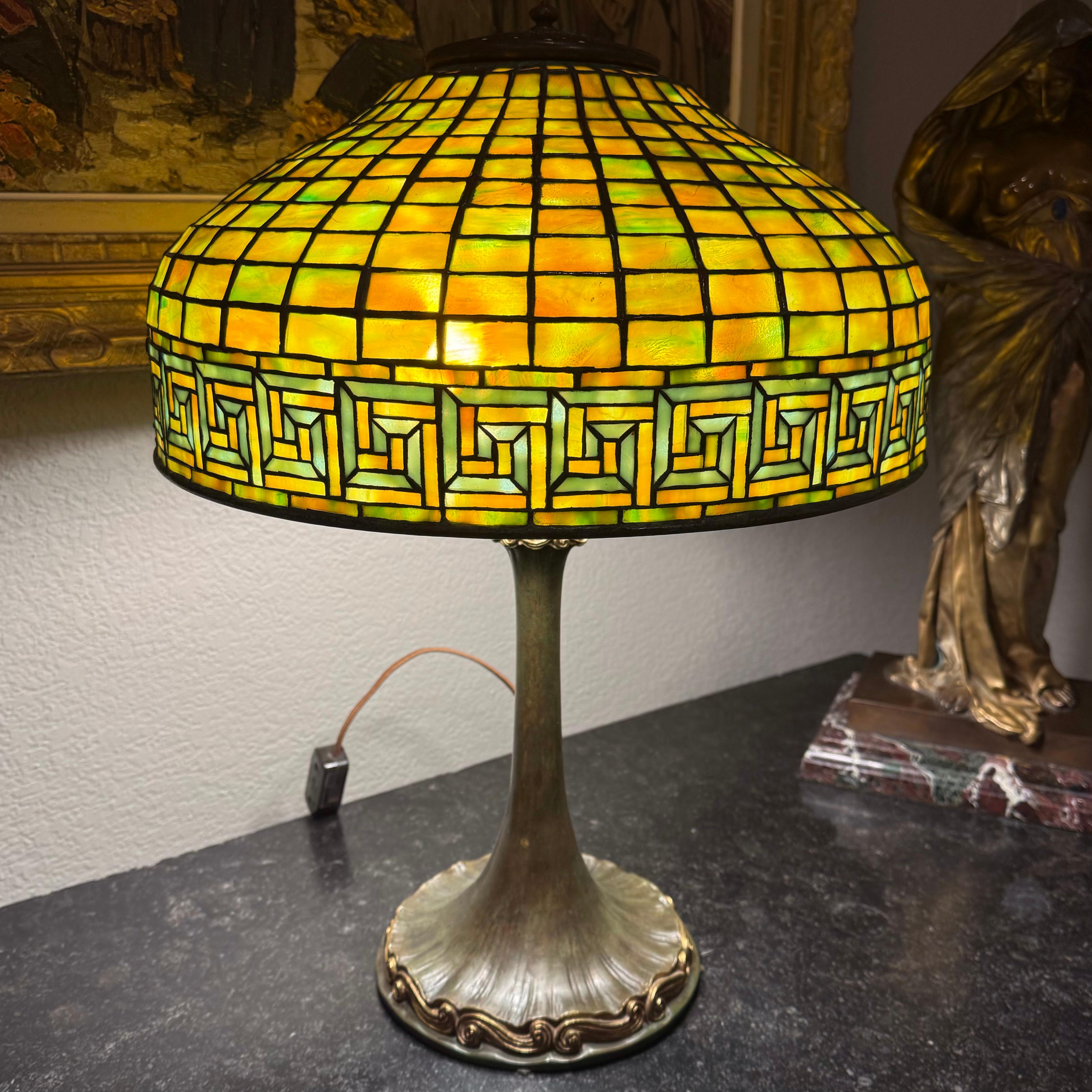 Tiffany Studios New York
Greek Key table lamp

New York, Circa 1910
Leaded glass, patinated and gilt bronze
Dimensions: 21.75 Inches x 16 Inch diameter (55 x 41 cm)

Lamp features a Double Scroll (Wave) base.Impressed to shade 'TIFFANY STUDIOS 1444'