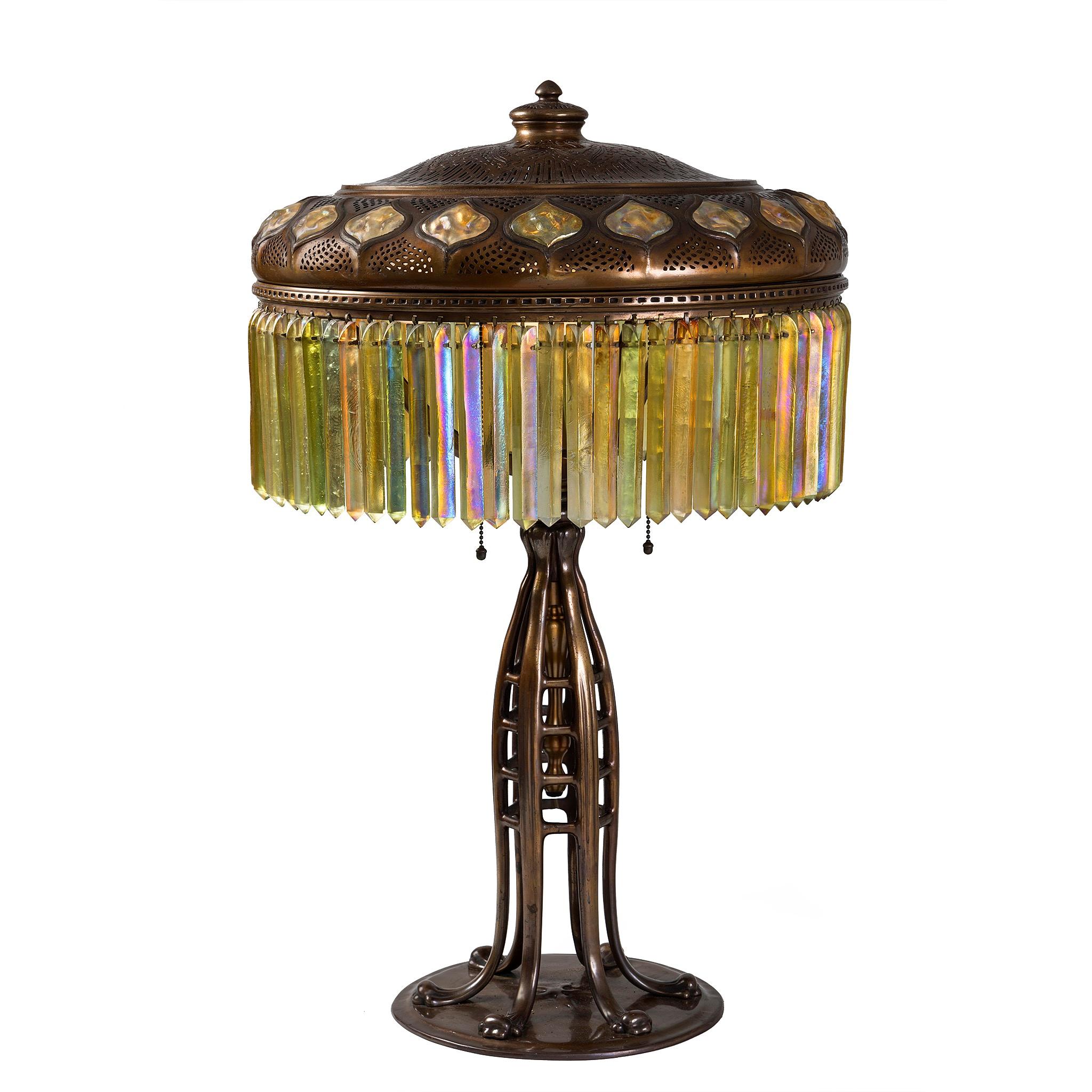 Esta exquisita lámpara prisma enjoyada de Tiffany Studios presenta un casquillo calefactor perforado adornado con un borde de veinte azulejos ojivales de dorso de tortuga. El motivo ojival, originario de los tejidos bizantinos del siglo XI, se