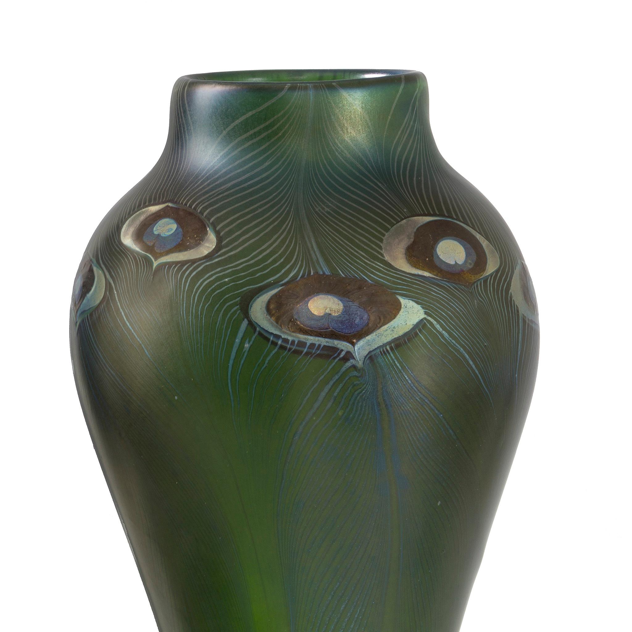 Questo maestoso vaso a forma di pavone di Tiffany Studios, a forma di balaustro, mostra un ipnotico disegno a piume tirate in vetro verde opaco e blu iridescente. Gli 