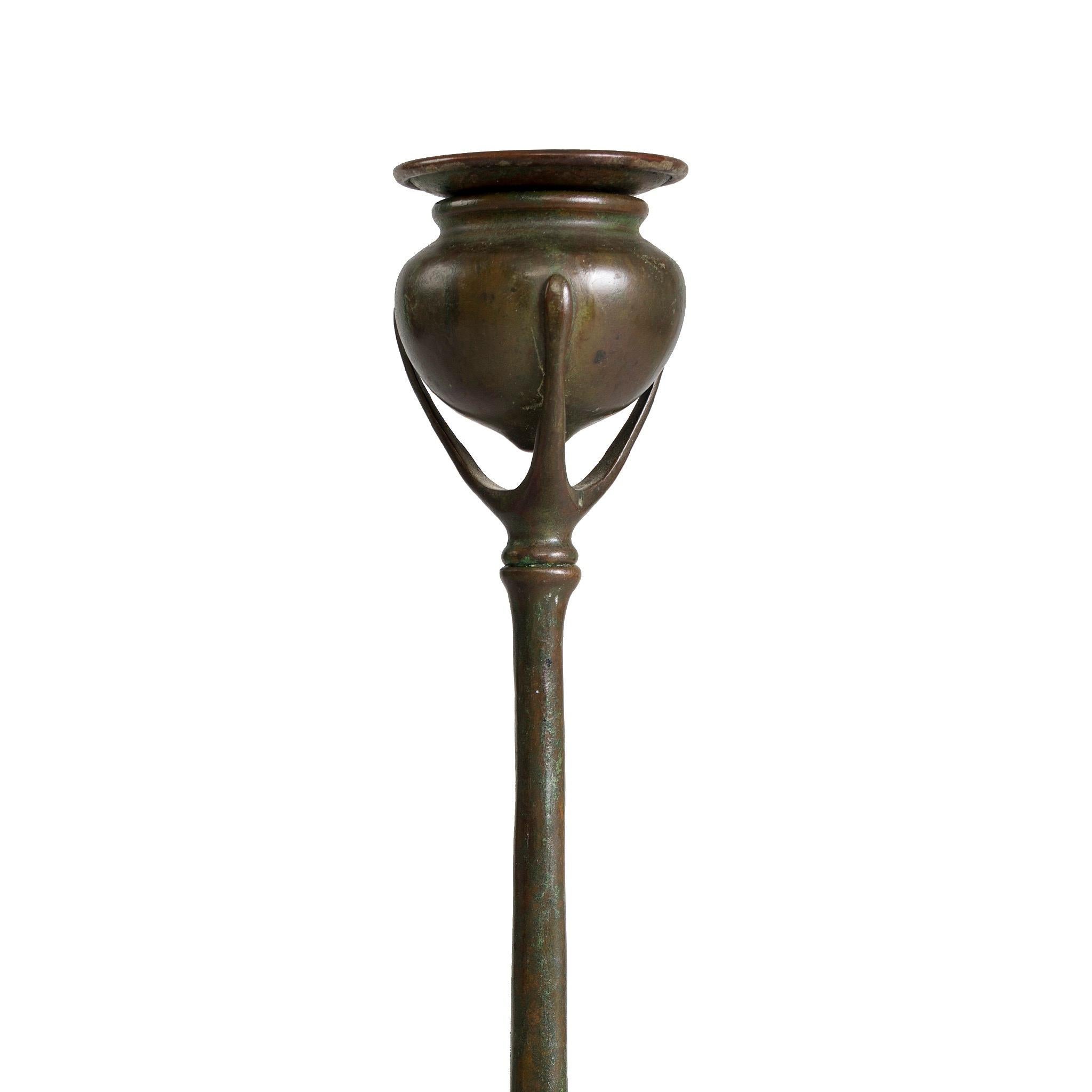 This exquisite pair of bronze candlesticks by Tiffany Studios New York, have three root feet leading to a slender, tapering stem. The stem supports a bulbous candle cup with bronze bobeche inserts. The design of the root candlesticks was inspired by