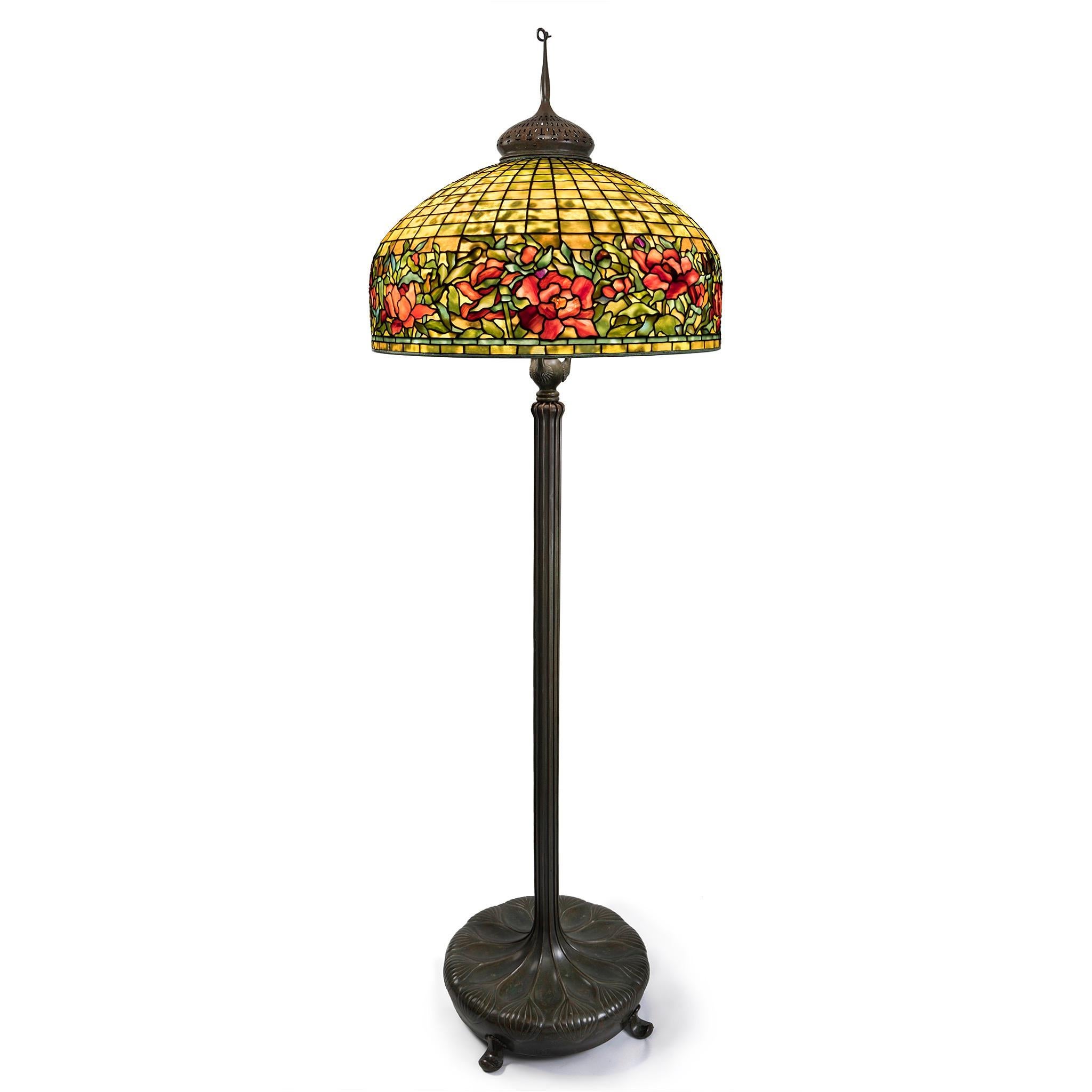 A Tiffany Studios peony border leaded glass and bronze senior floor lamp. The vibrantly colored shade with striated orange geometric upper register and with lower border comprising a band of peonies in various stages of development in variegated