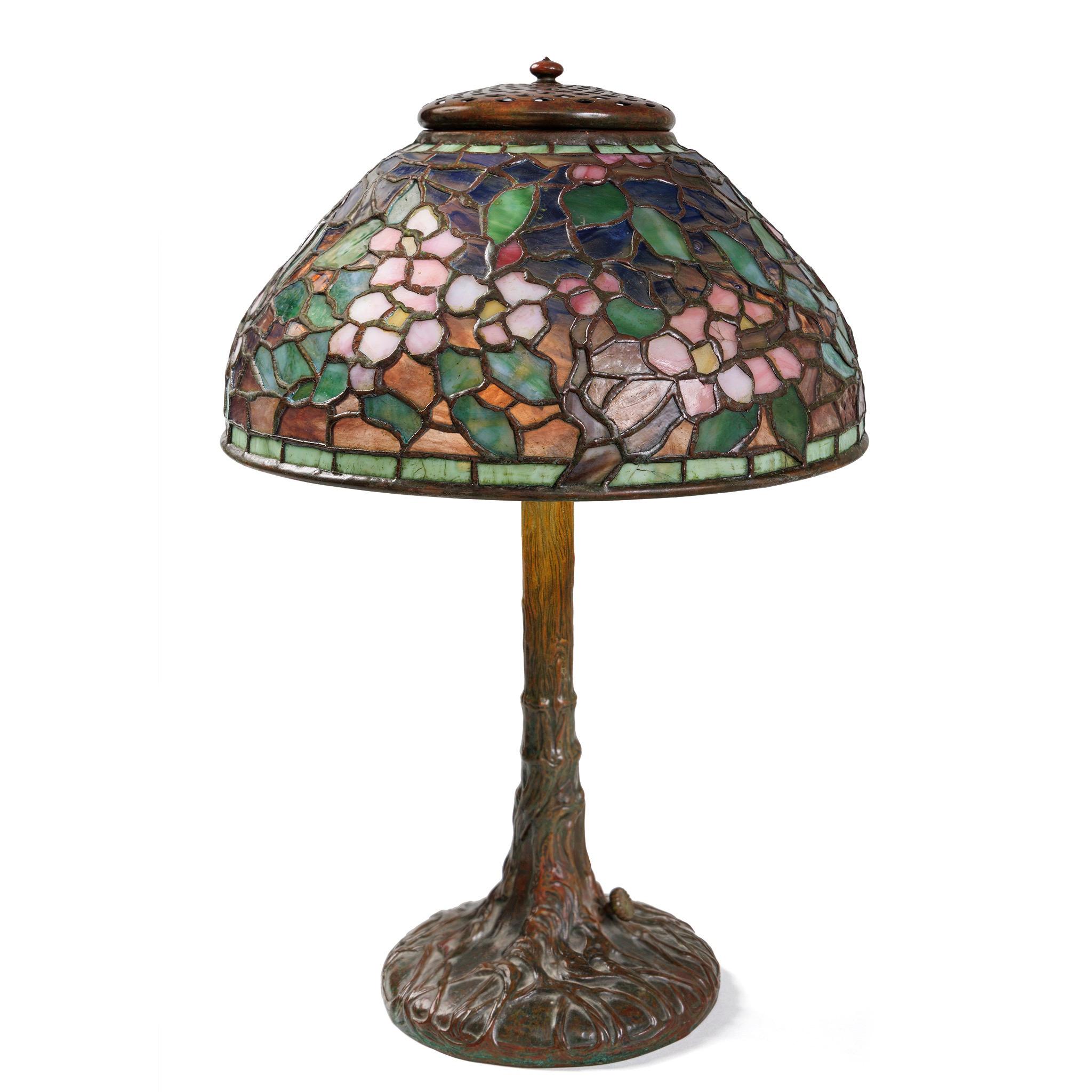 White blossoms tinged with gentle pinkish hues stand against a light blue sky that gradates into a green meadow horizon in this Tiffany Studios New York 