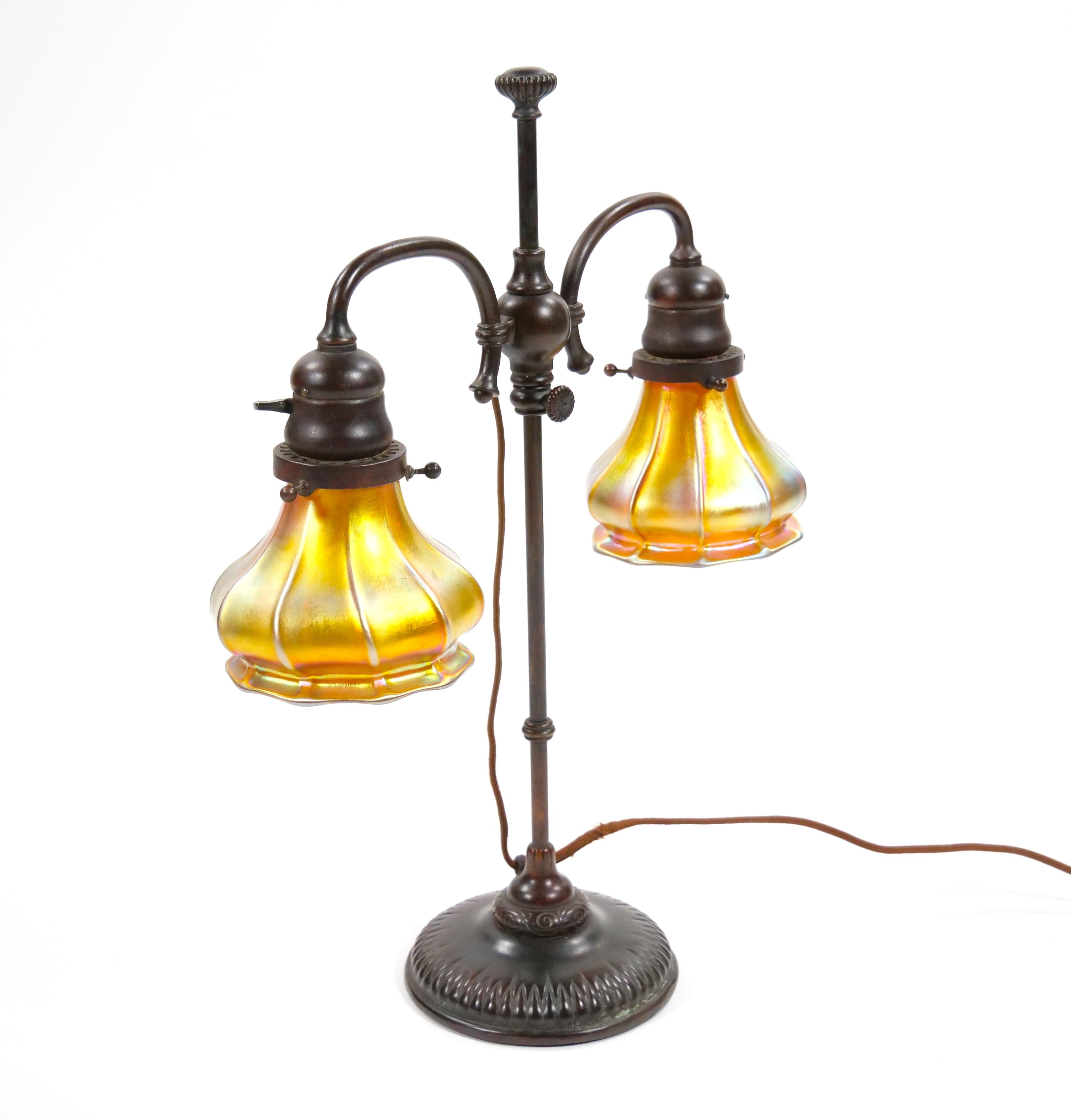 This exquisite Tiffany Studios Bronze & Art Glass Lamp is a remarkable piece of early 20th-century craftsmanship, embodying the timeless elegance and artistry synonymous with Tiffany Studios. Featuring a double-arm student lamp design, the lamp is
