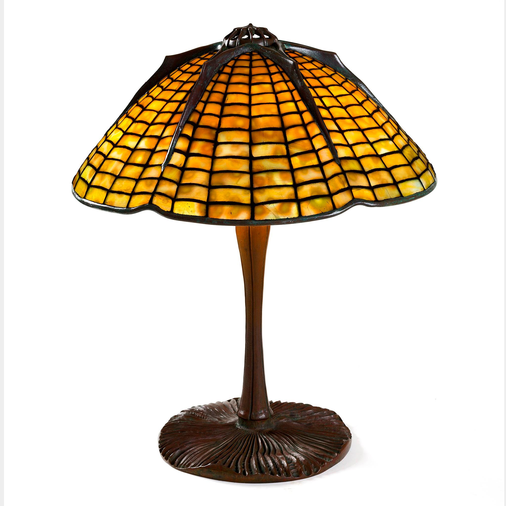 This Tiffany Studios New York glass and bronze “Spider” table lamp features a mottled golden glass shade of undulating golden hues, atop a patinated bronze “Inverted Mushroom” base. With Gothic, arachnid-type raised veins spreading from the clawed