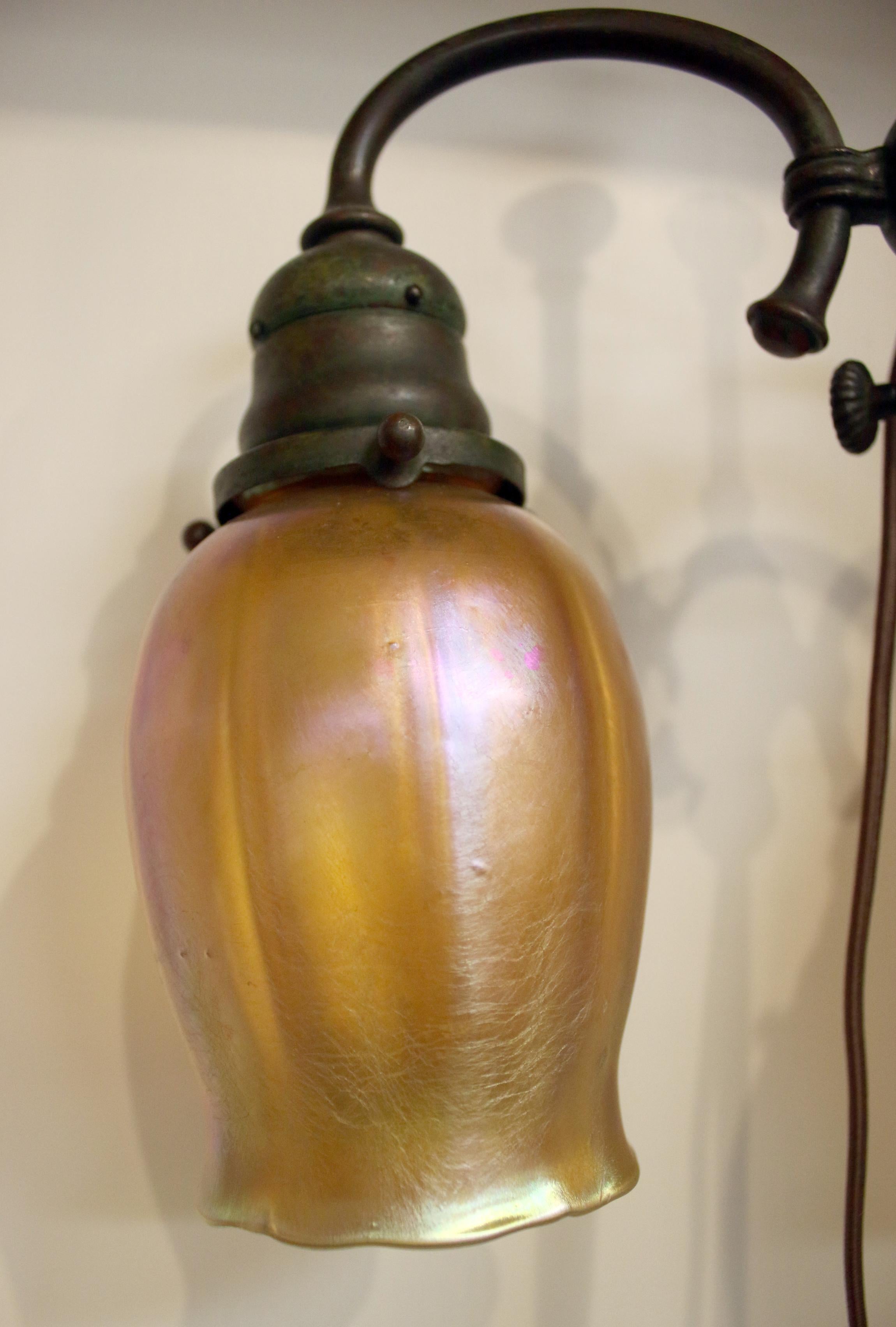 Two bell shaped art glass signed iridescent shades are supported by an adjustable bronze two arm base with bell sockets. The twin paddle knob sockets are stamped GE CO. The base is signed Tiffany Studio New York 304,T
circa 1900. Original glass and