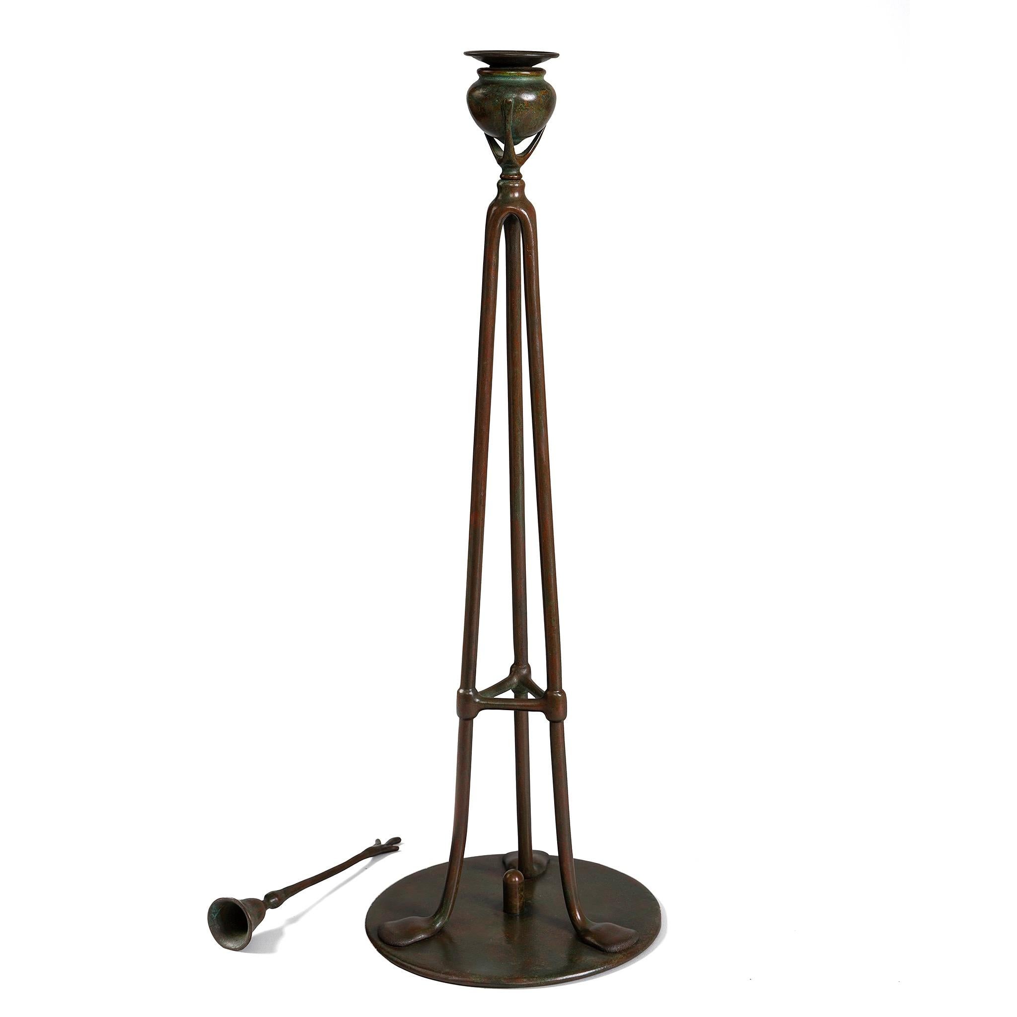 A Tiffany Studios New York glass and bronze “Tripod” candlestick, featuring a round ball top with a bobeche insert. The patinated bronze base includes a removable bronze snuffer. The Tripod candlestick was based on the tripod perfume burners of