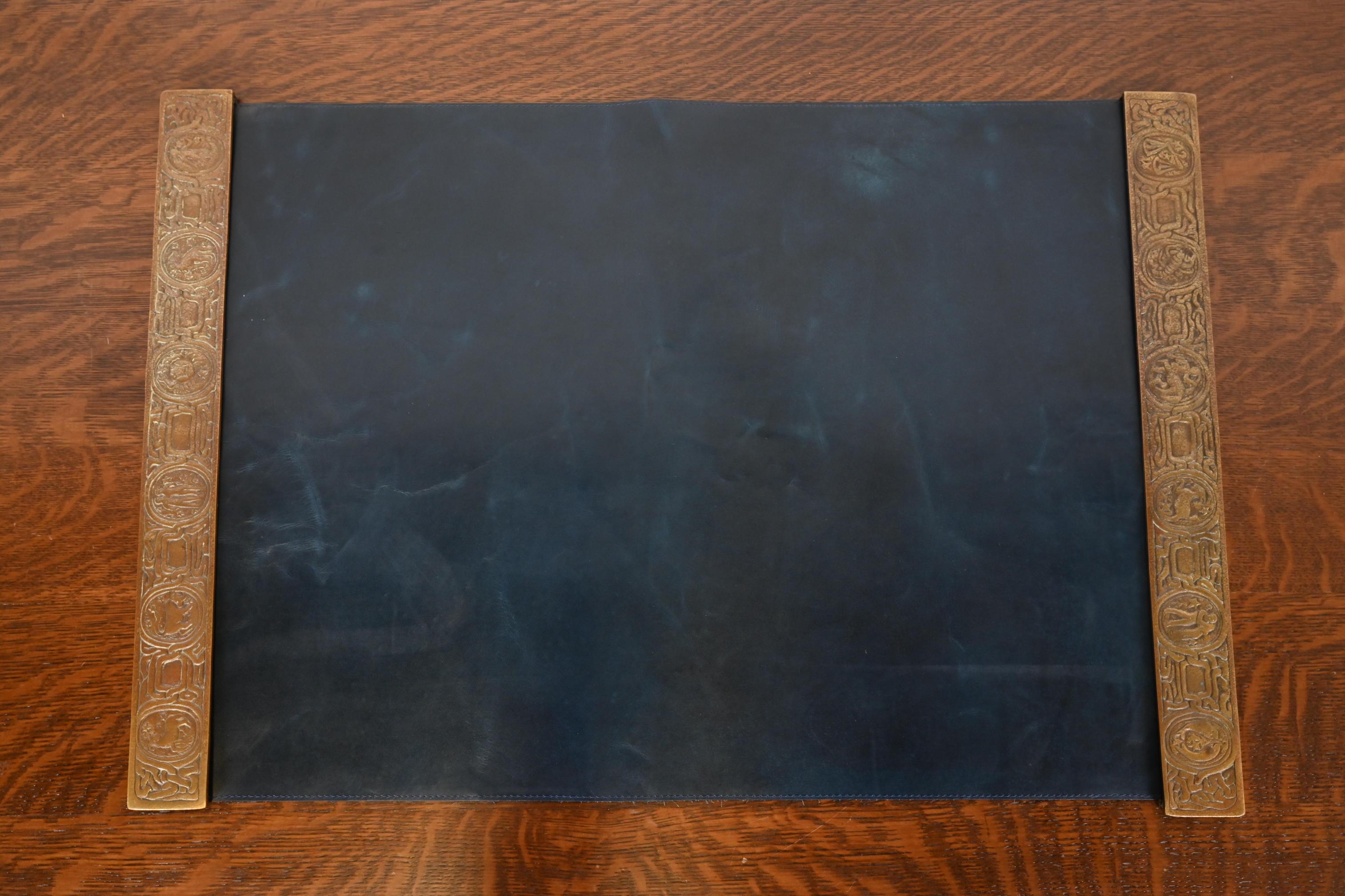 A gorgeous pair of Art Deco or Arts & Crafts period bronze blotter ends featuring symbols of the Zodiac, with a custom blue leather desk blotter.

By Tiffany Studios (blotter ends signed to the underside)

New York, USA, Early 20th Century

Each