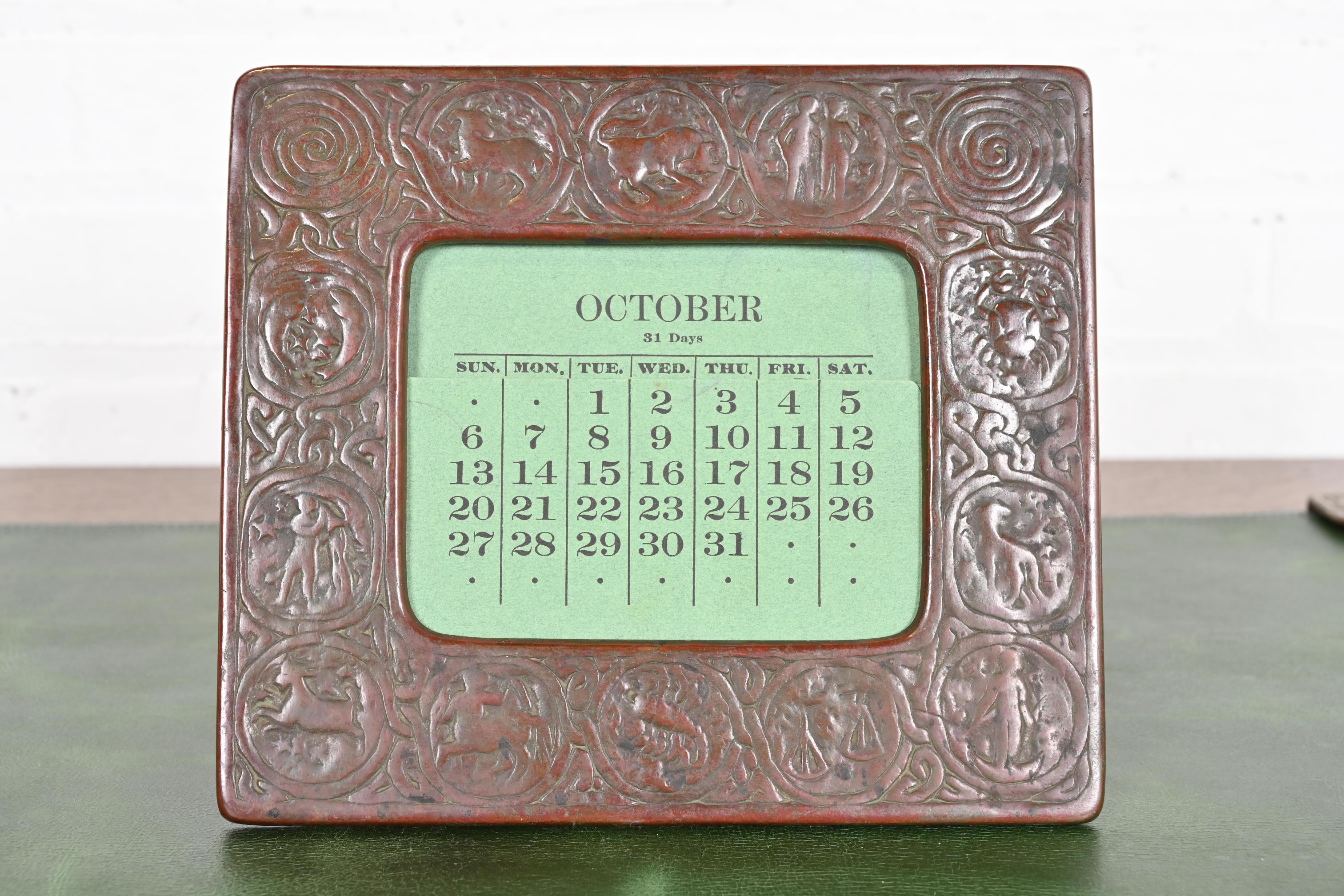 Ein wunderschöner Art Deco oder Arts & Crafts Bronze Tischkalenderhalter oder Bilderrahmen mit Symbolen des Zodiacs.

Von Tiffany Studios (signiert auf der Rückseite)

New York, USA, Anfang des 20. Jahrhunderts

Maße: 8,13 