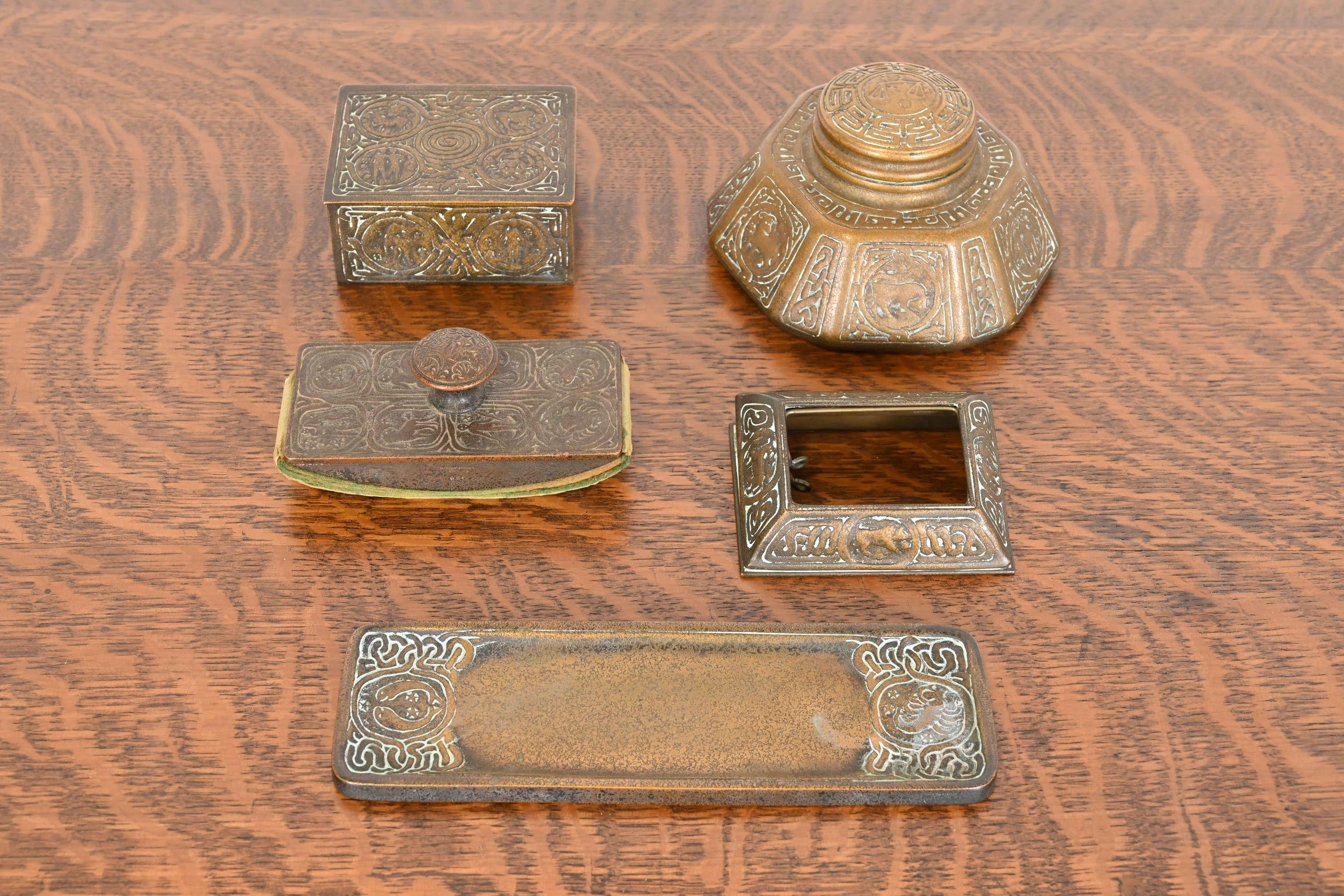 An outstanding bronze desk set featuring Zodiac designs. The five-piece set includes: desk calendar holder or picture frame, large inkwell, pen tray, desk box, and rocker blotter.

By Tiffany Studios

New York, USA, Early 20th
