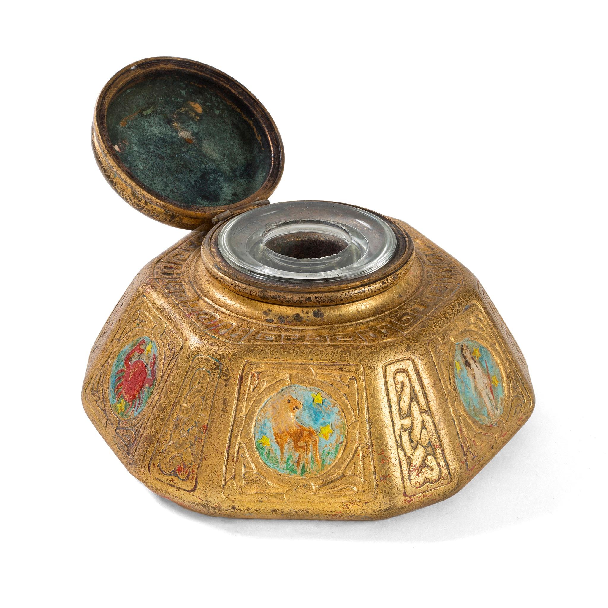 A gilt bronze “Zodiac” inkwell by Tiffany Studios New York. The inkwell features intricate pseudo-Celtic patterning interspersed with circular elements in sky blue, each of which features a stylized depiction of one of the 12 signs of the Zodiac,
