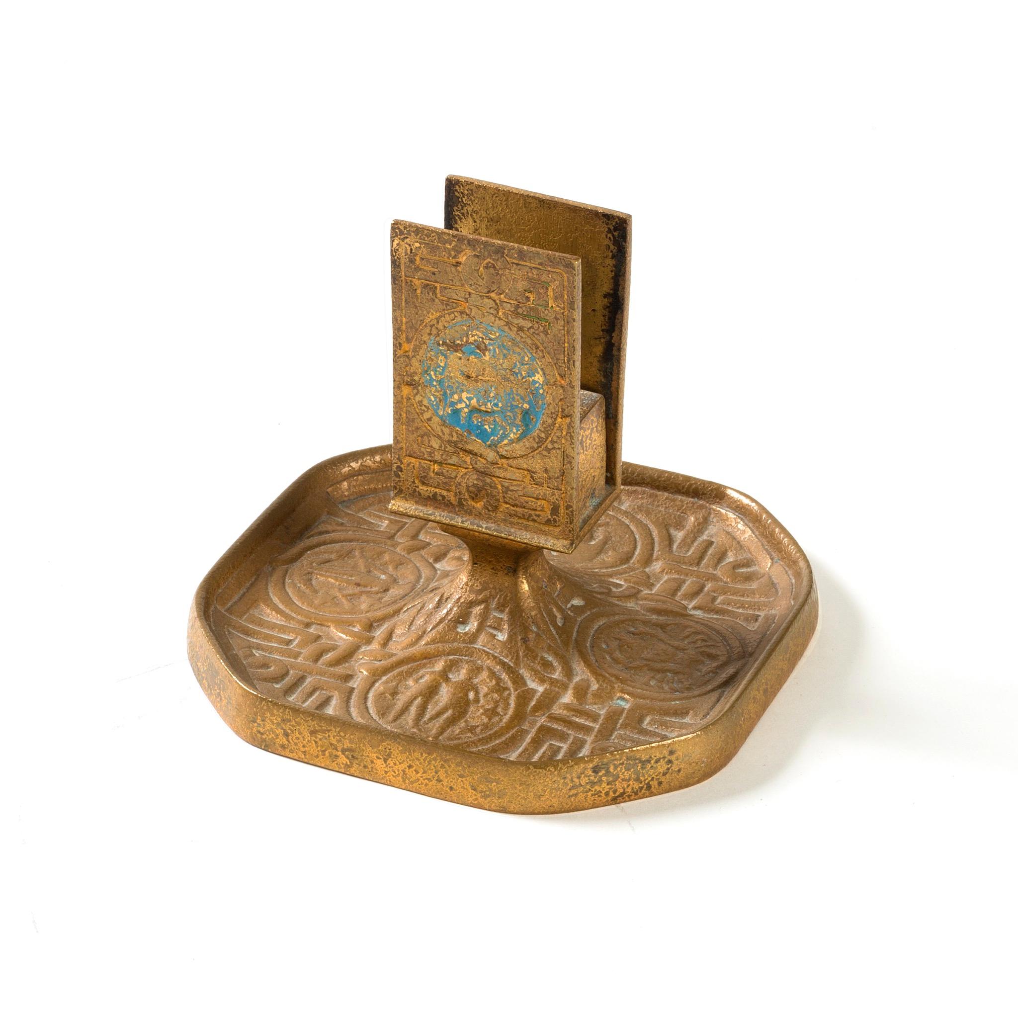A gilt bronze “Zodiac” match box holder by Tiffany Studios New York. The match box holder features intricate pseudo-Celtic patterning interspersed with circular elements in sky blue, each of which features a stylized depiction of one of the 12 signs
