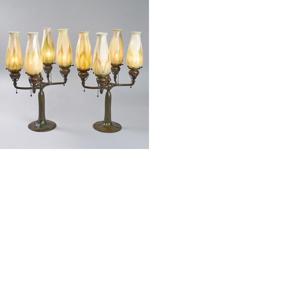A pair of Tiffany Studios New York glass and bronze electrified candelabra, each one featuring; four iridescent white and green Favrile glass shades with a 