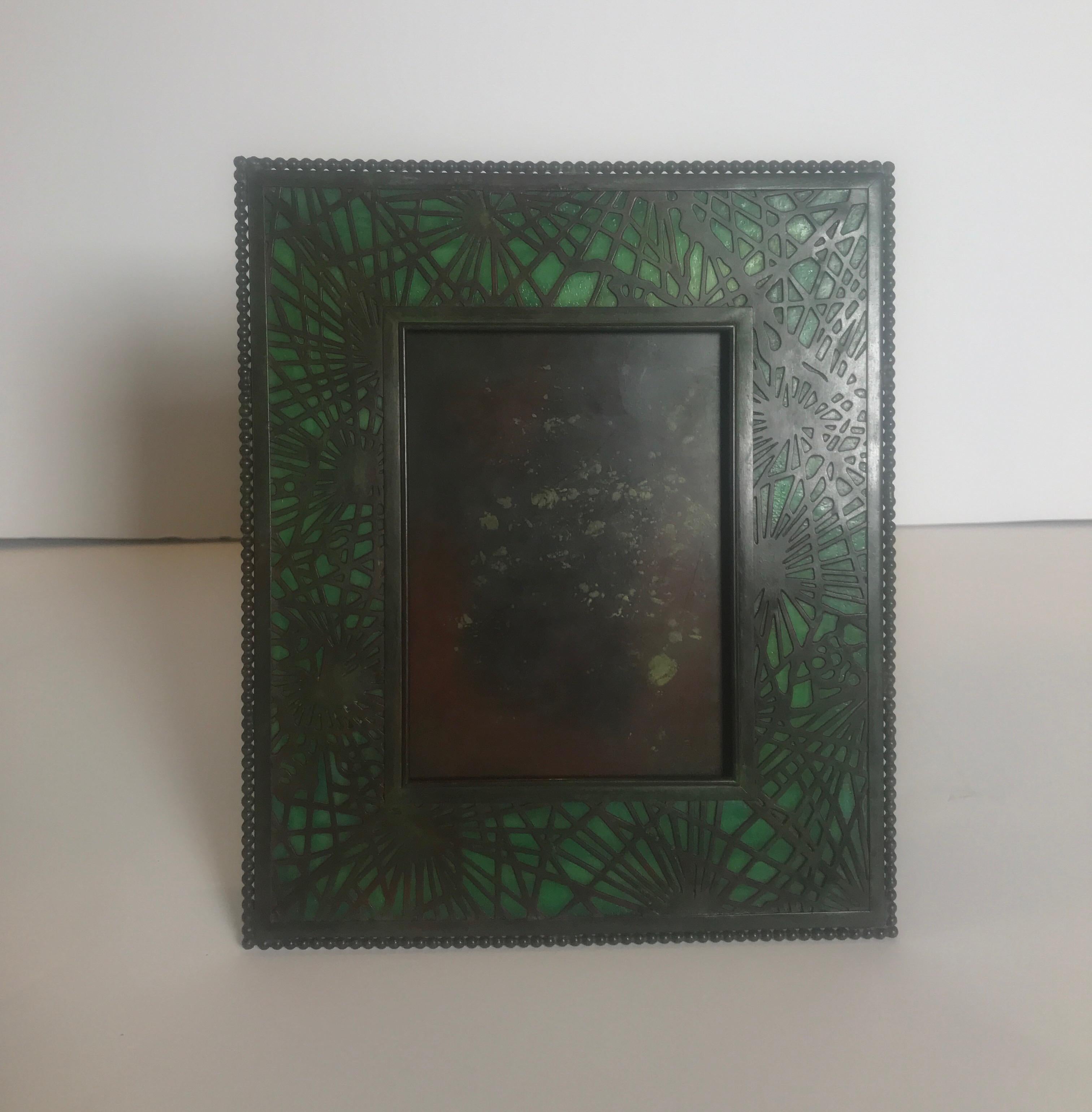 Tiffany studios pine needle frame. Etched metal design, in the pine needle pattern, is set against a green striated glass and has a desirable green-brown patina finish. Frame is finished with a single row of bronze beads to inner and outer edge.