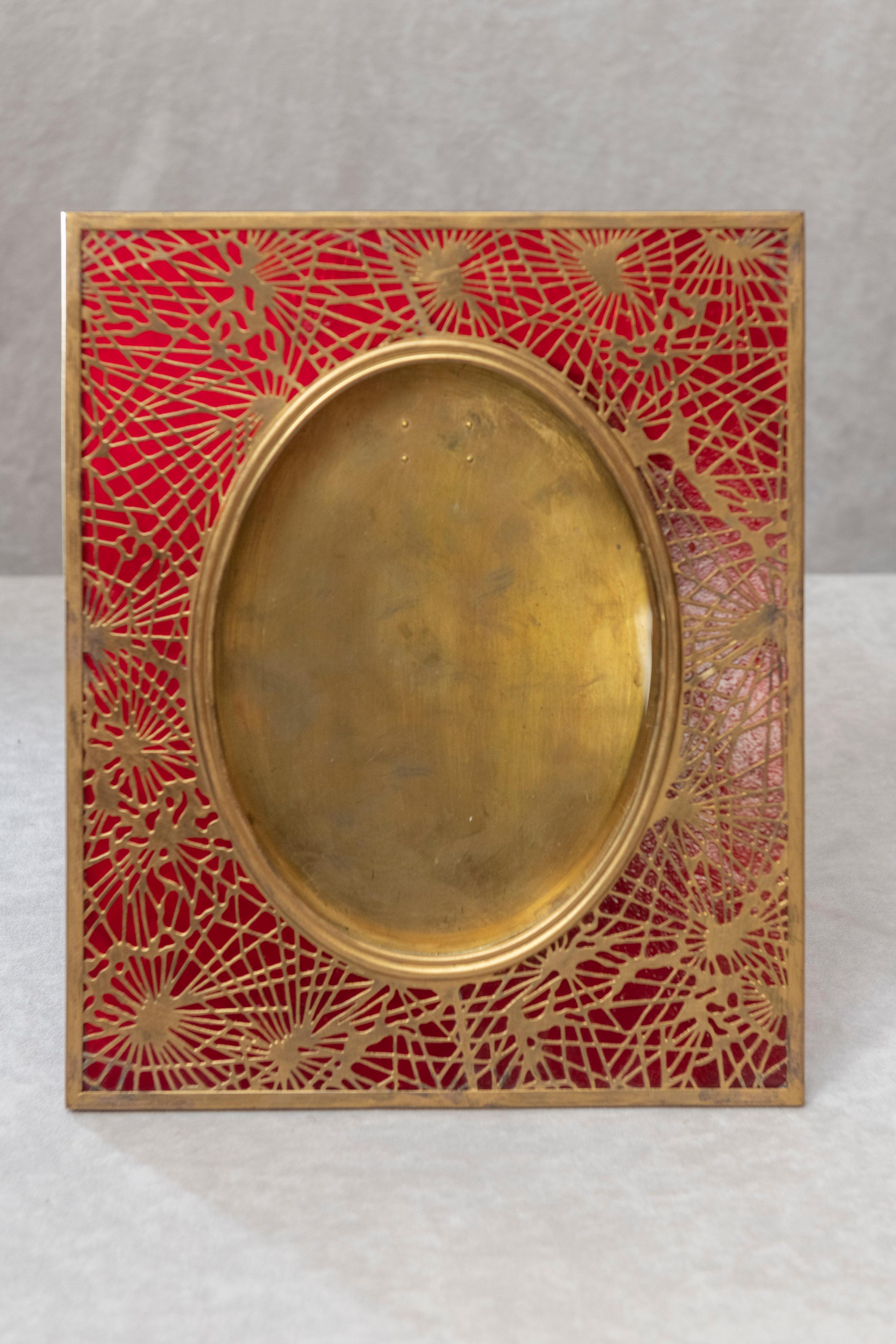 This beautiful original Tiffany Studios picture frame has ruby red glass and gilt metal, all done in their popular pine needle pattern. Normally the glass is green or amber. This one is rather exotic and has a rich look with the red background glass