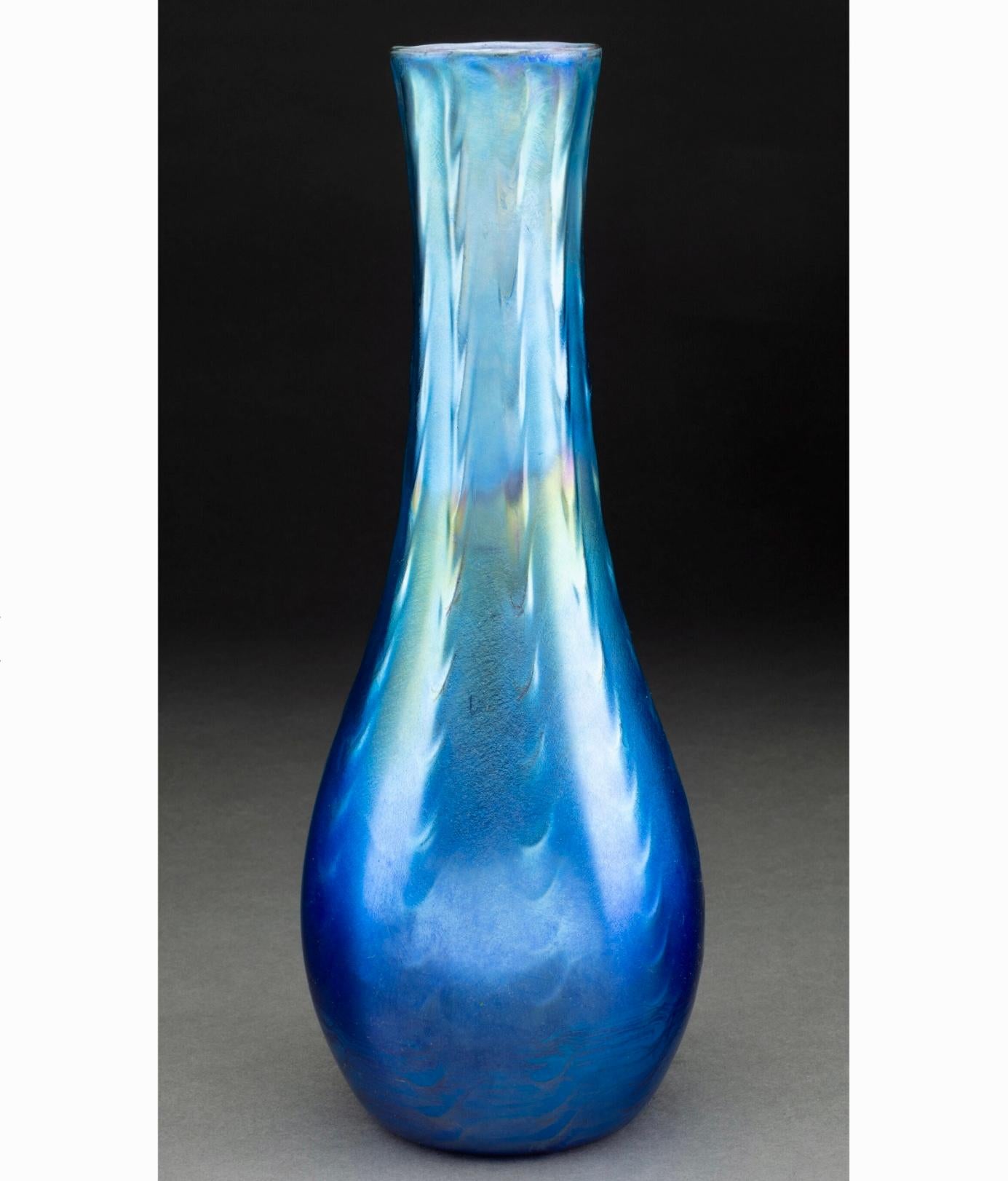 Vaso in vetro Studio Nouveau di Tiffany Studios con decorazioni a coste, blu e iridescente.
Vaso a coste, 1910 circa
USA, New York
Vetro di Favrile
12,25 pollici (31,1 cm) X 4,3 pollici di diametro 
Marchi: 1539-9666M, A.L.C. Tiffany-Inc,