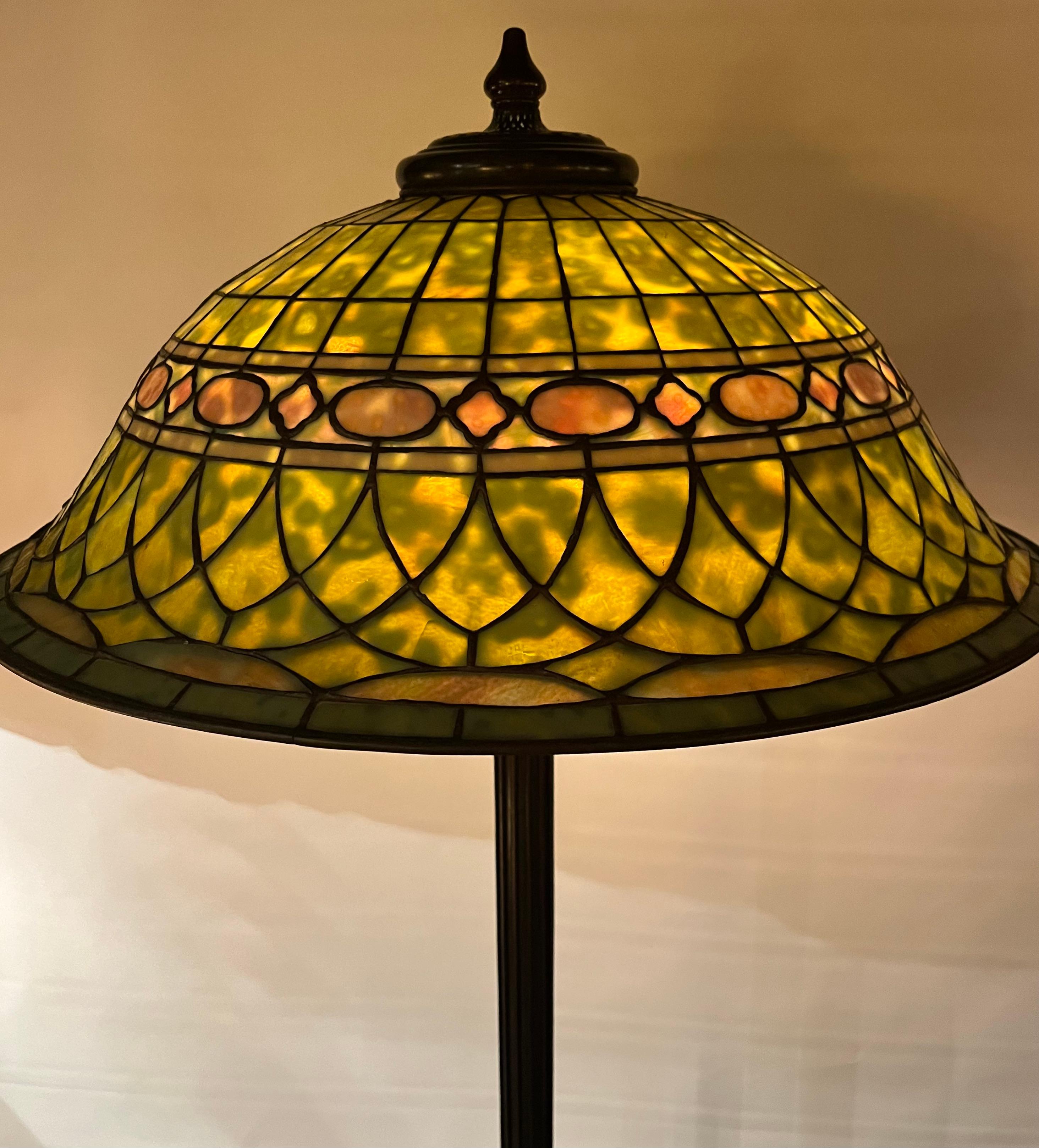 This vintage early 20th century Tiffany Studios floor lamp is decorated with a “Roman” design leaded lampshade. The shade is signed  “Tiffany Studios, New York” & numbered “1564”. The shade consists of a beautiful blend of mottled colors within this