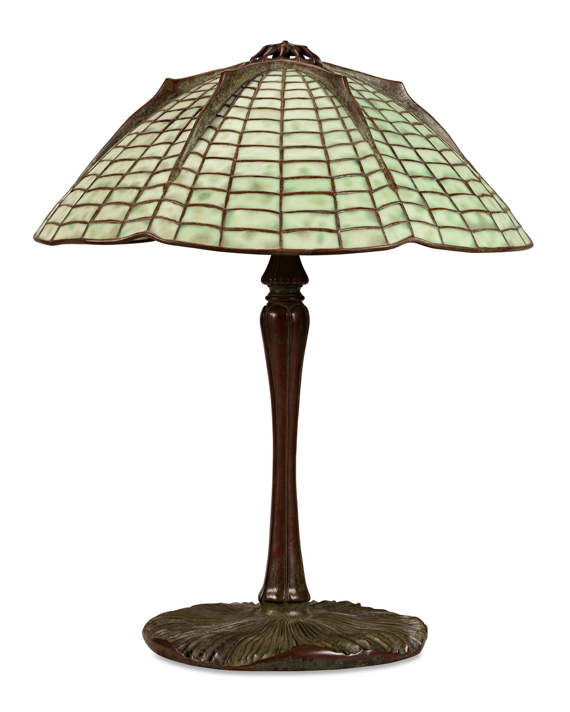 This Tiffany Studios geometric leaded glass and bronze table lamp features the iconic Spider shade and its original complementary Mushroom bronze base. The unique form of the spider and web-inspired shade combines with the soft green and yellow