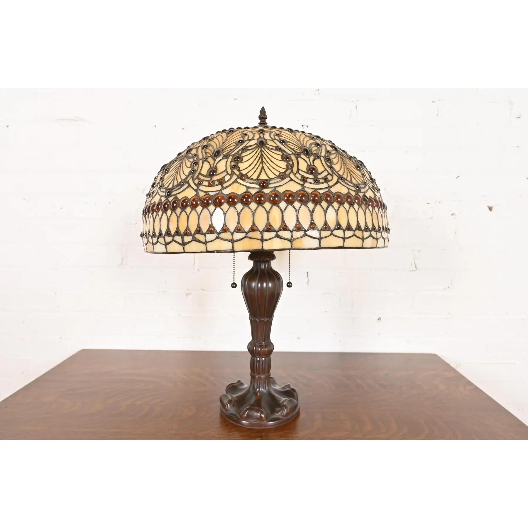 Magnifique lampe de table de style Arts & Crafts avec abat-jour en verre teinté orné de bijoux.

À la manière des studios Tiffany 

USA, Circa Late 20th Century

Dimensions : 17,5 