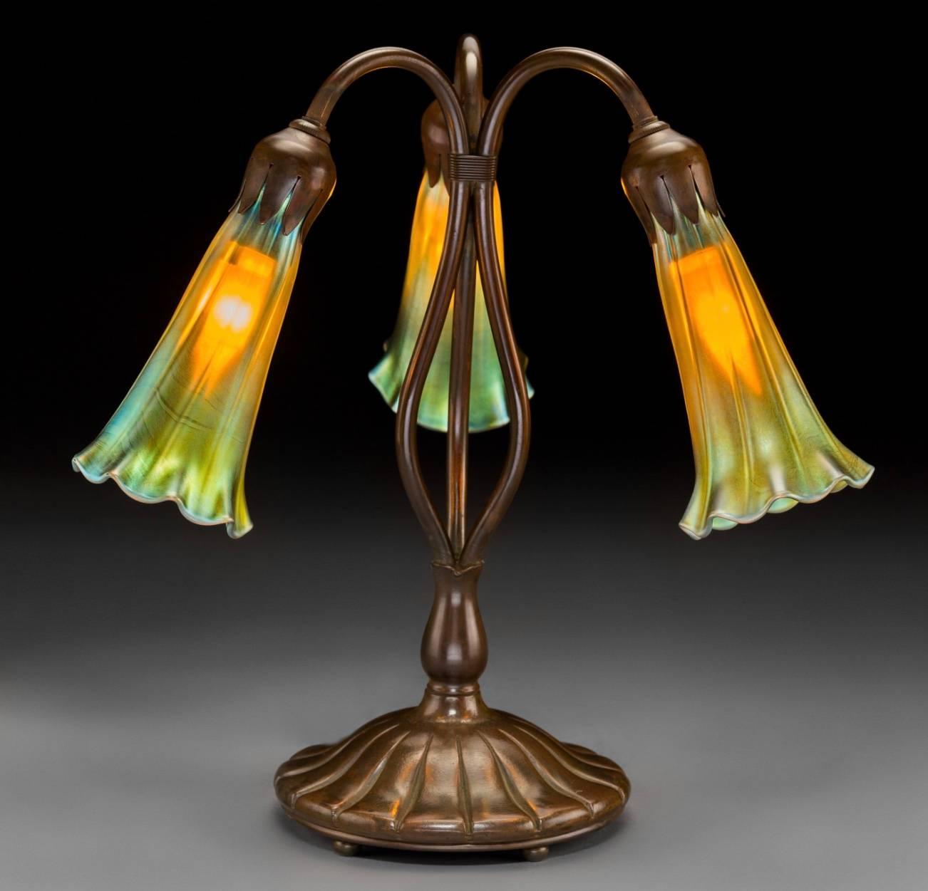 Tiffany Studios Style gold Favrile glass and bronze three-light lily lamp. Quality reproduction TSNY signed TIFFANY STUDIOS NEW YORK 319 on base and etched L.C.T on shades. 20th century.

Height. 12 Inches.

Excellent condition.

Images by Heritage