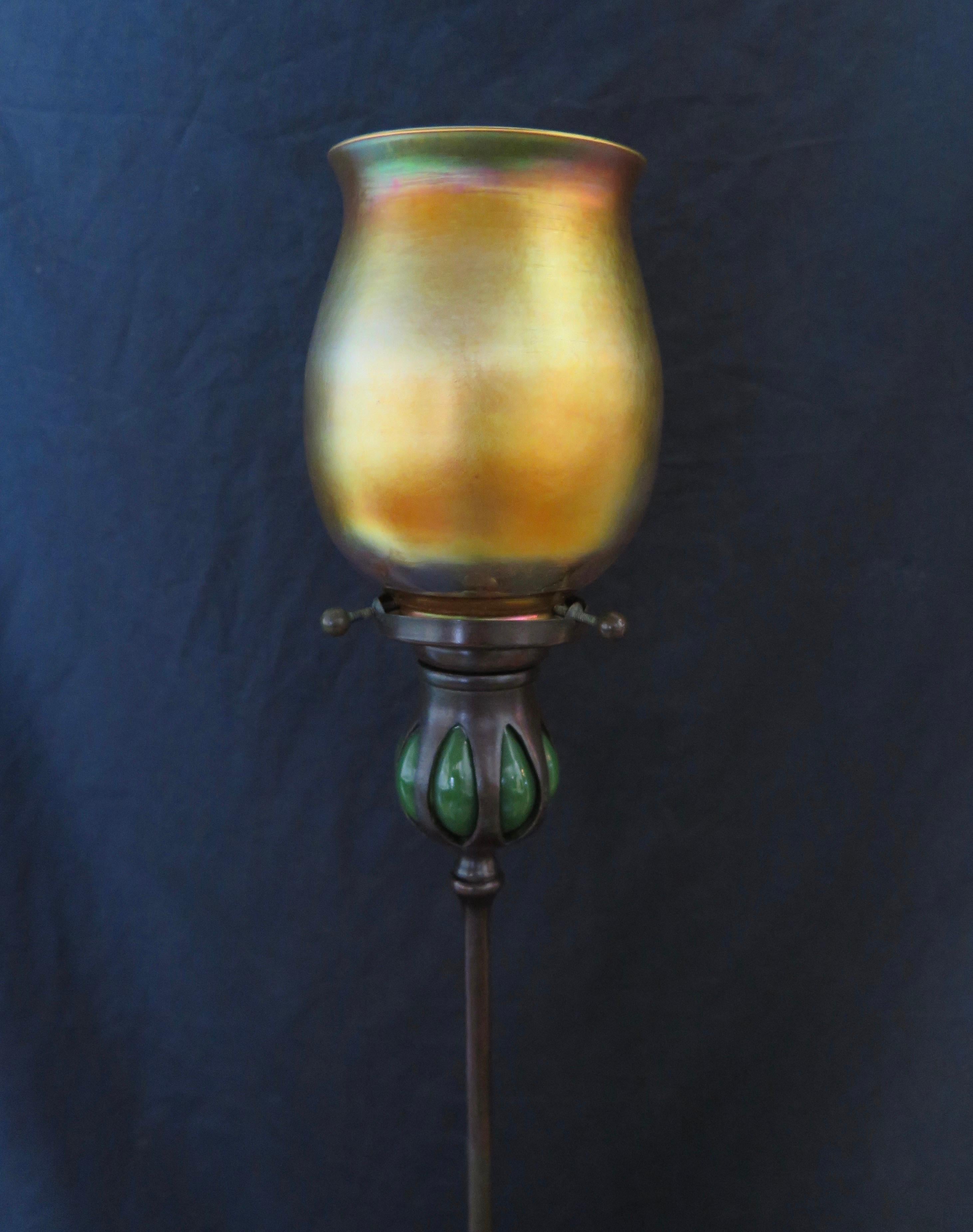 This Tiffany Studios patinated tall candlestick features a blown out green glass candle cup. This candle cup contains an original shade holder with 3 “set” screws & holds a beautiful iridescent gold Tiffany favrile art glass tulip shade. The patina
