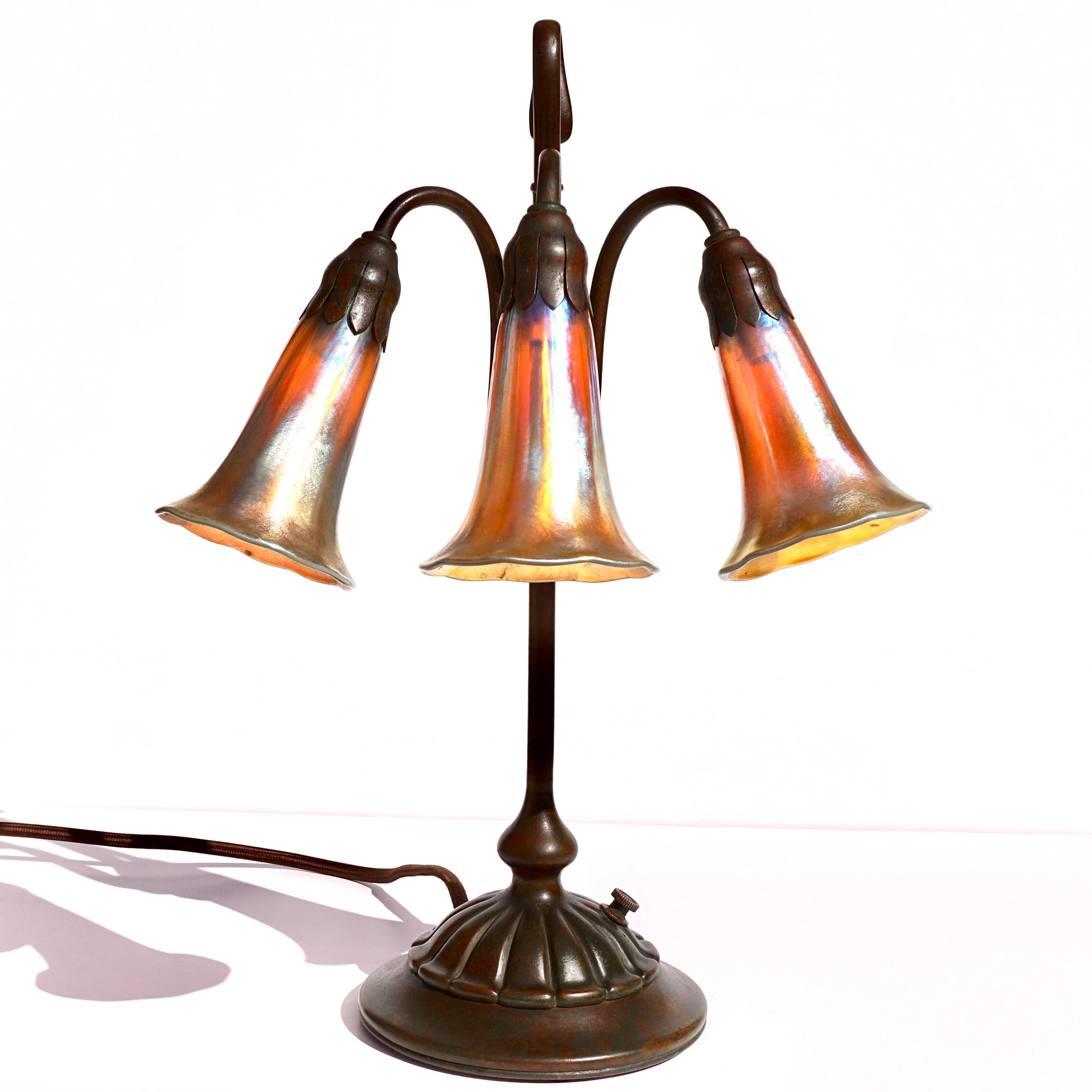 Tiffany Studios three light lily table lamp. 
Three Light Lily lamp
circa 1905
Patinated bronze, with three Tiffany favrile glass shades, each shade marked 'L.C.T. Favrile', base stamped 'TIFFANY STUDIOS NEW YORK 306' to underside.

Condition: