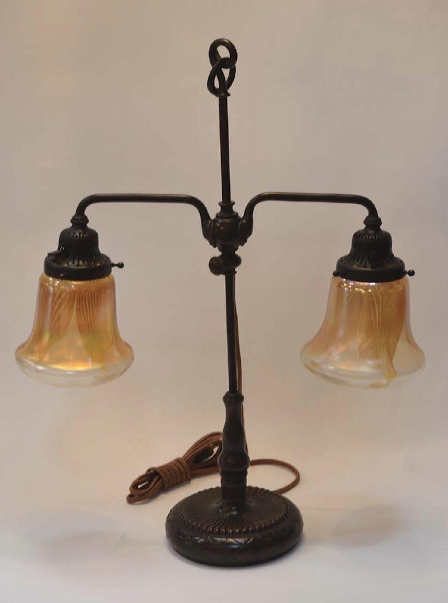 Tiffany Studios two light bronze favrile table lamp. Two bell-shaped favrile glass signed iridescent shades supported by an adjustable bronze two-armed base with bell sockets. The base is signed by Tiffany Studios New York. 