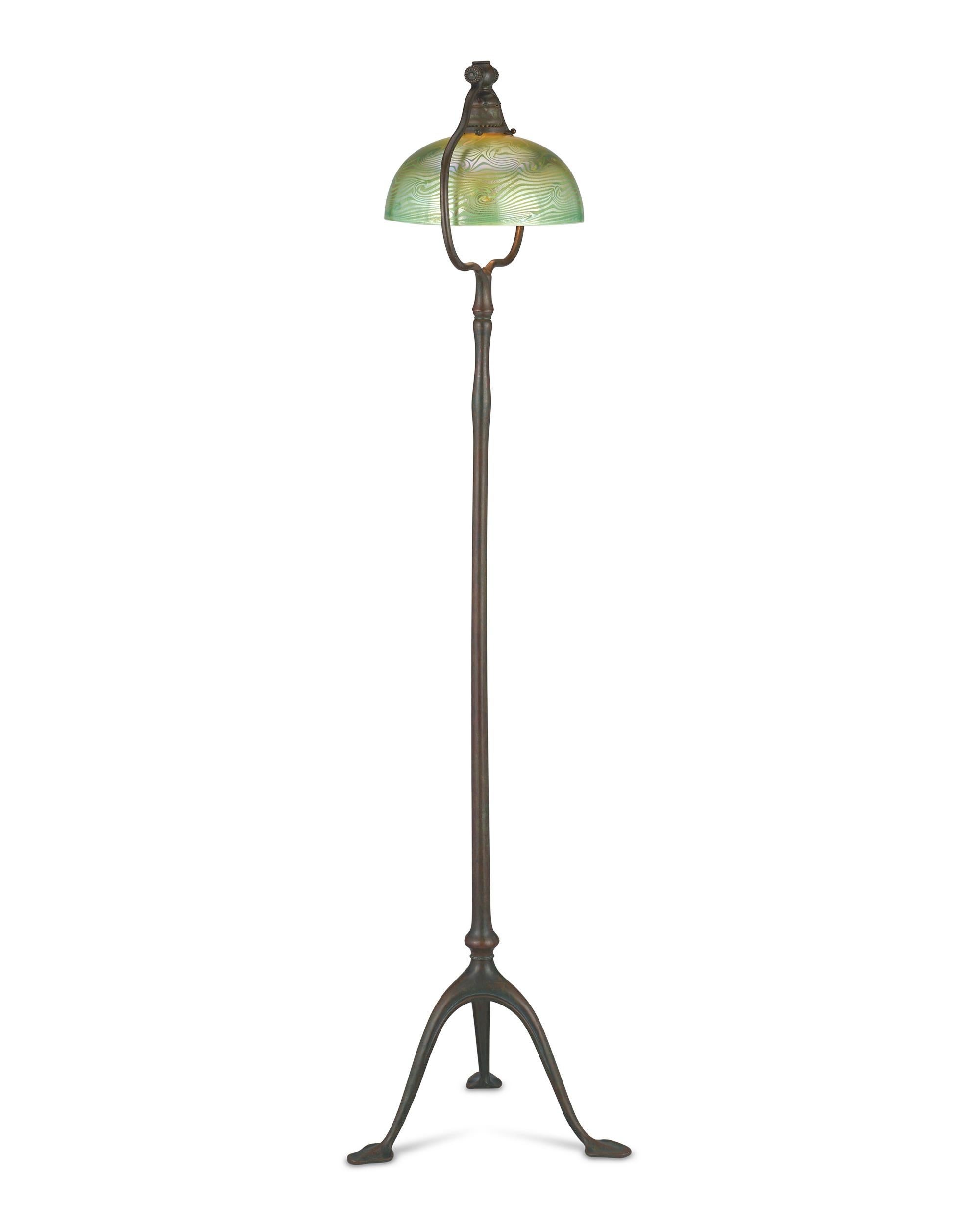 This exceptional floor lamp by Tiffany Studios features an iconic dome shade crafted from the firm's legendary Favrile glass, complemented by its original curved harp bronze base that accentuates the shade's overall form. Supported by three