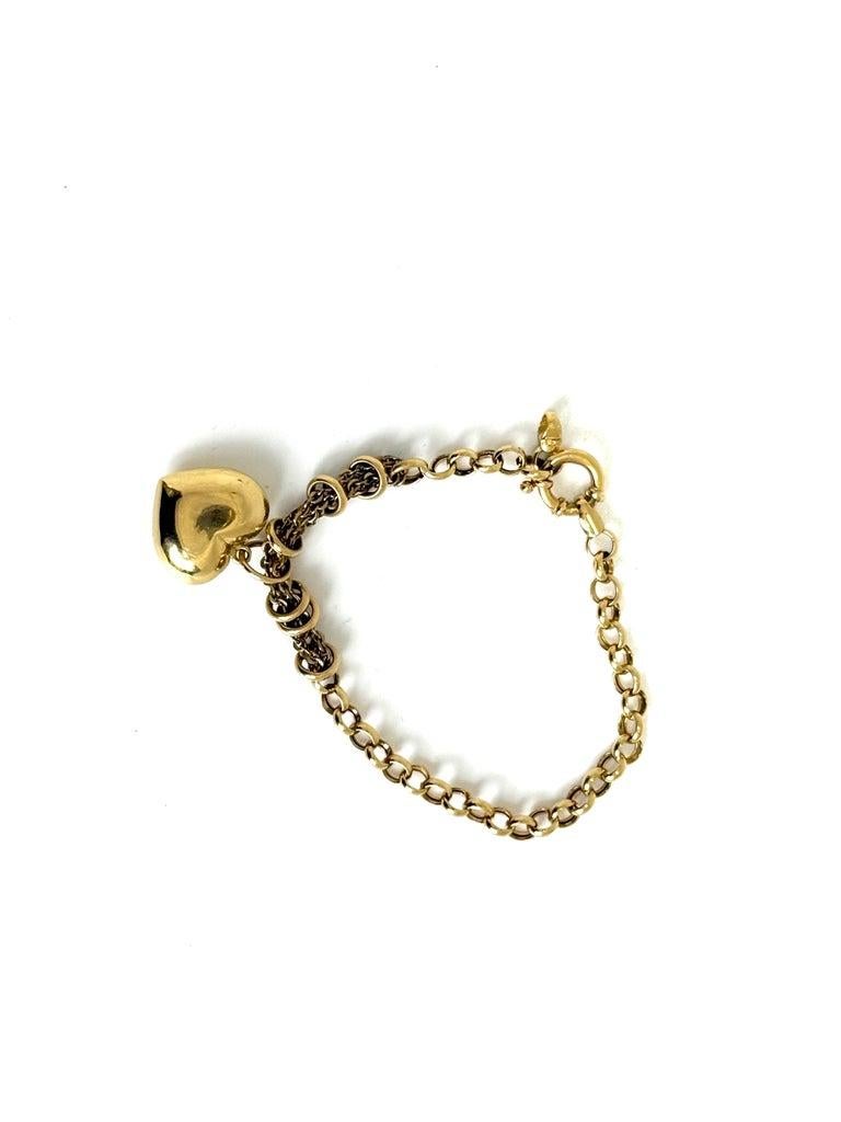 This elegant Tiffany-style bracelet is crafted in luxurious 18K yellow gold and features a bold, polished puffed heart charm that brings a romantic and timeless touch. The bracelet’s design blends classic round links with intricate woven rope