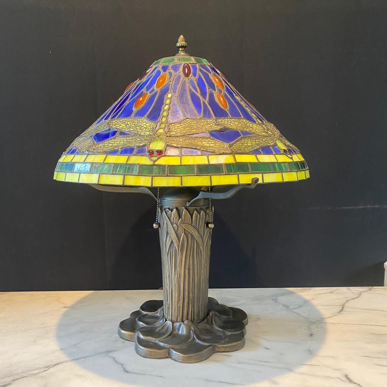  Lampe de table de style Art Nouveau Tiffany avec abat-jour en verre au plomb à motifs de libellules avec panneaux en verre teinté et base en quenouille en bronze. Une belle lampe de table en vitrail avec sa base en forme de nénuphar et de gaines de